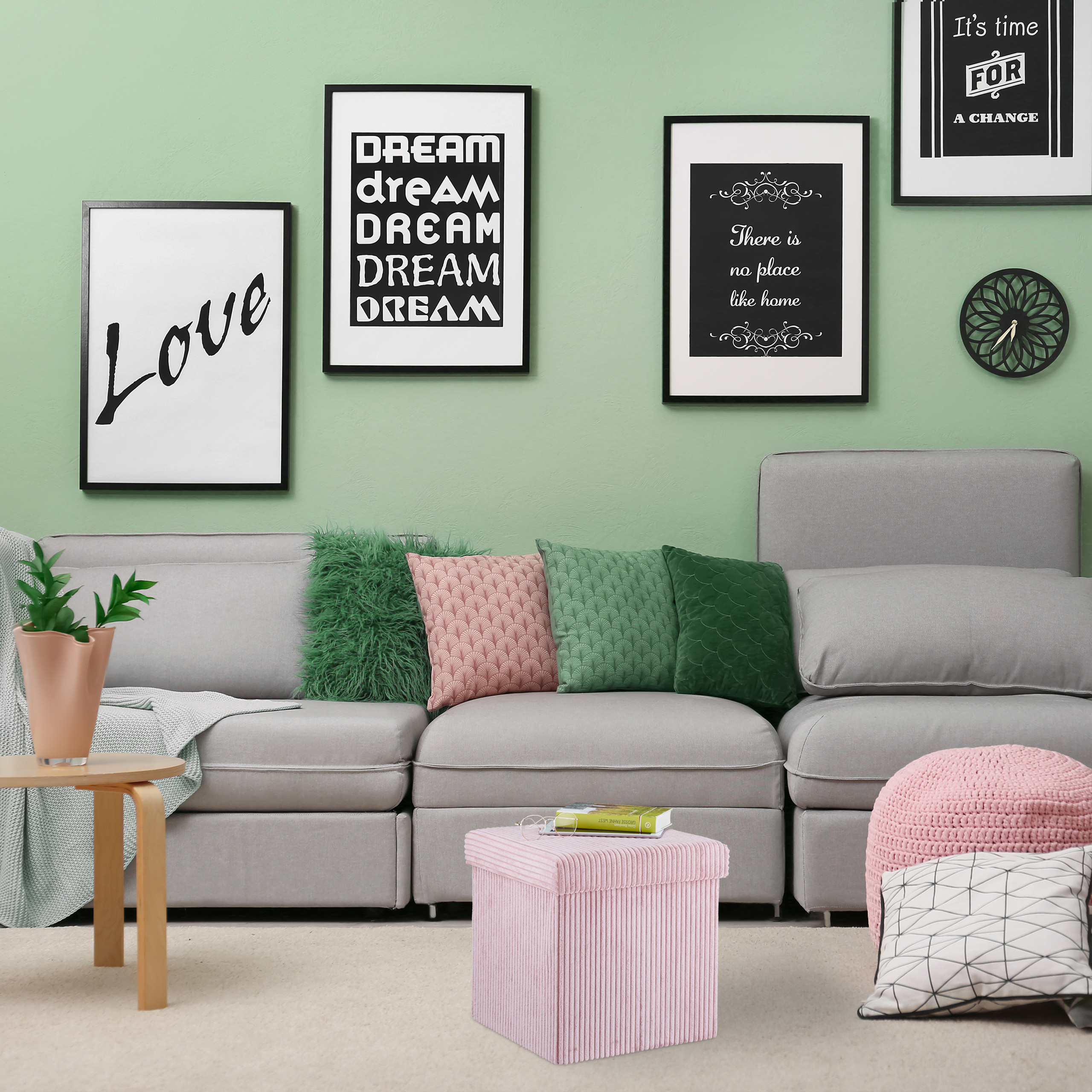Ein graues Sofa steht an einer hellgrünen Wand mit gerahmten Bildern und Kissen in Grün und Rosa.