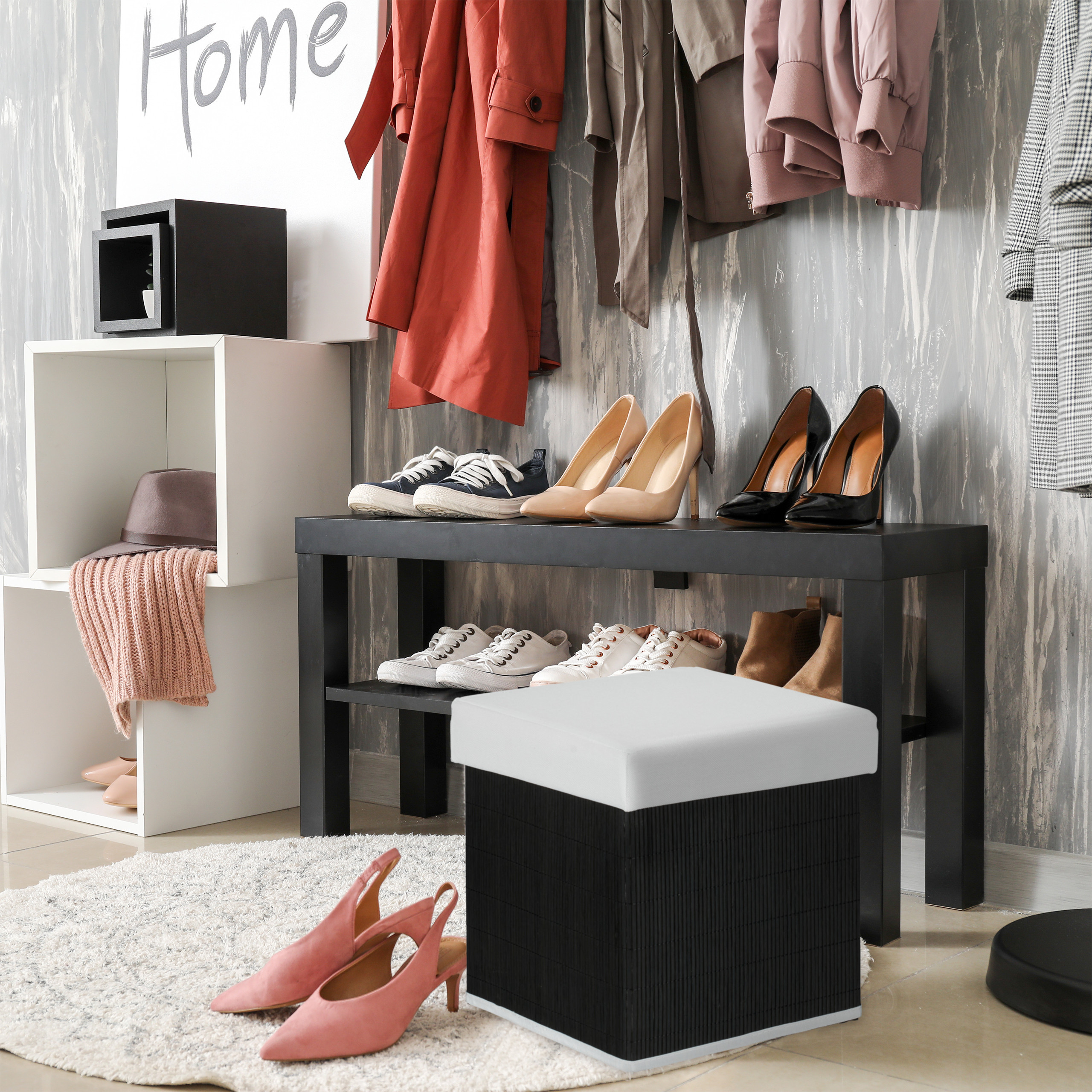 Moderne Flurgarderobe mit Bank, Schuhen, Mänteln, Hocker und Dekorelementen vor grauer Wand.