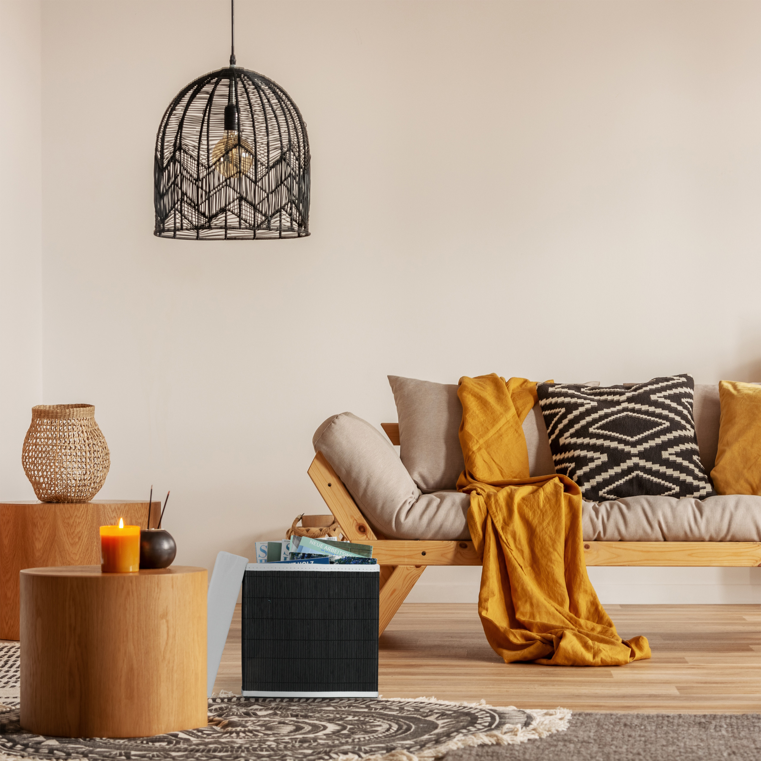 Gemütliches Wohnzimmer mit Holzsofa, gelber Decke, gemusterten Kissen und schwarzer Hängeleuchte an weißer Wand.