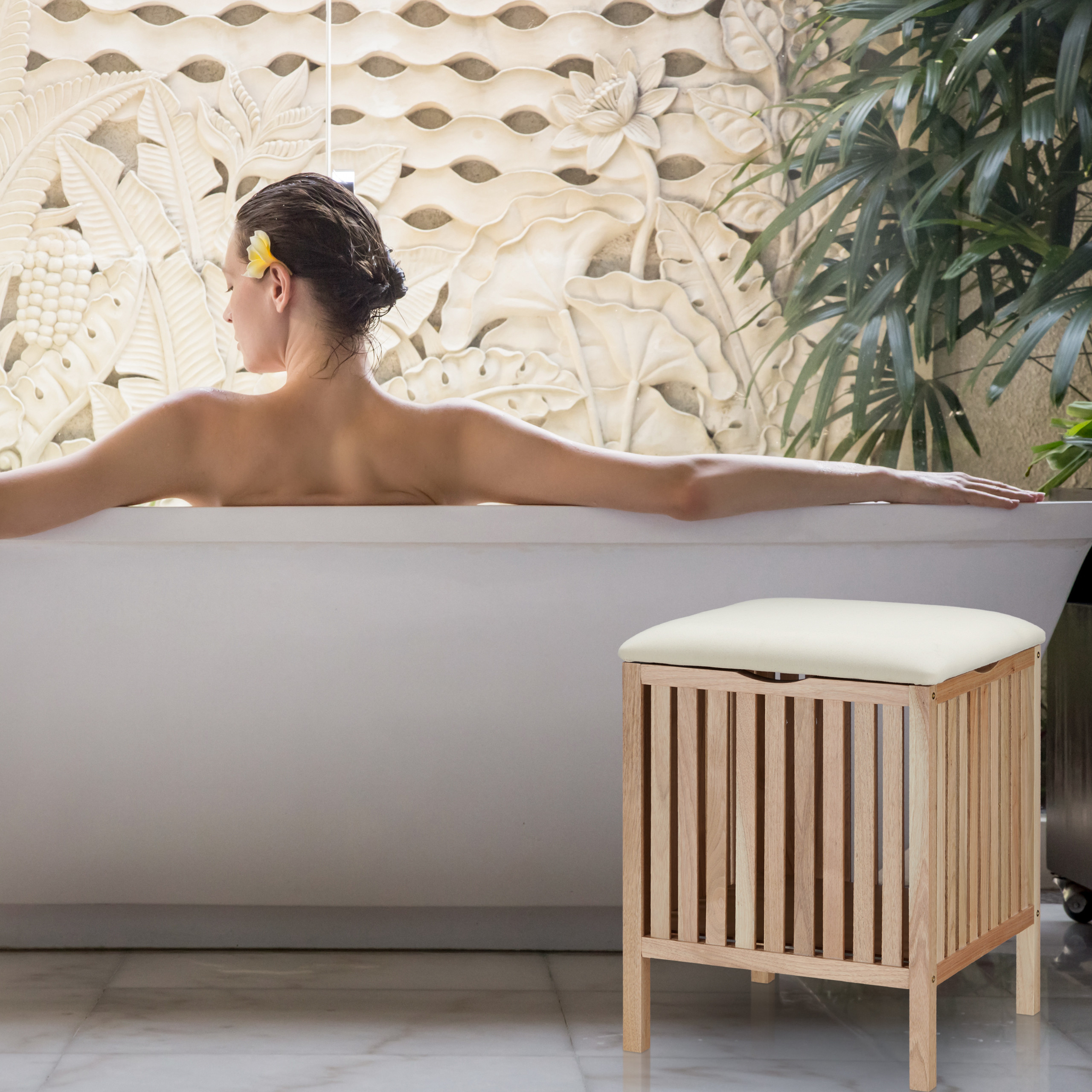 Frau sitzt in Badewanne vor geschnitzter Wand, daneben ein kleiner Holzhocker mit Kissen.