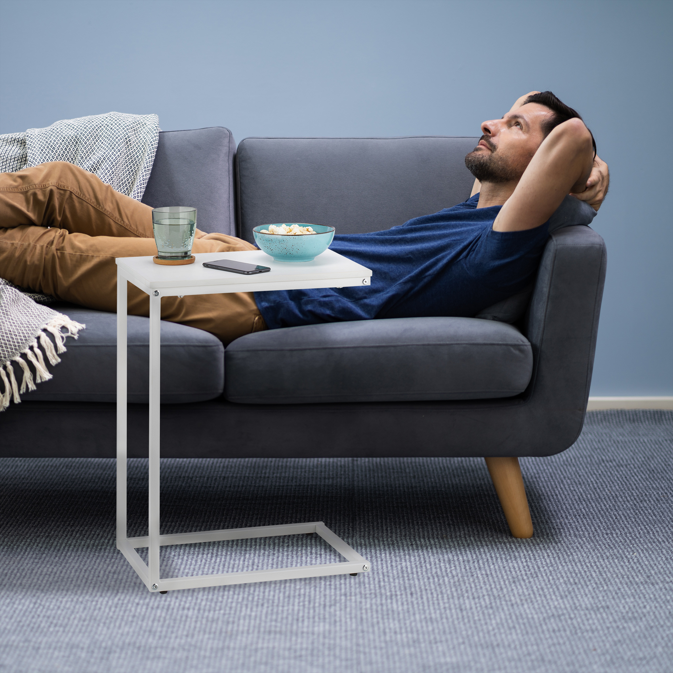 Ein Mann liegt entspannt auf einem grauen Sofa, neben ihm ein kleiner weißer Tisch mit Snackschale und Glas.