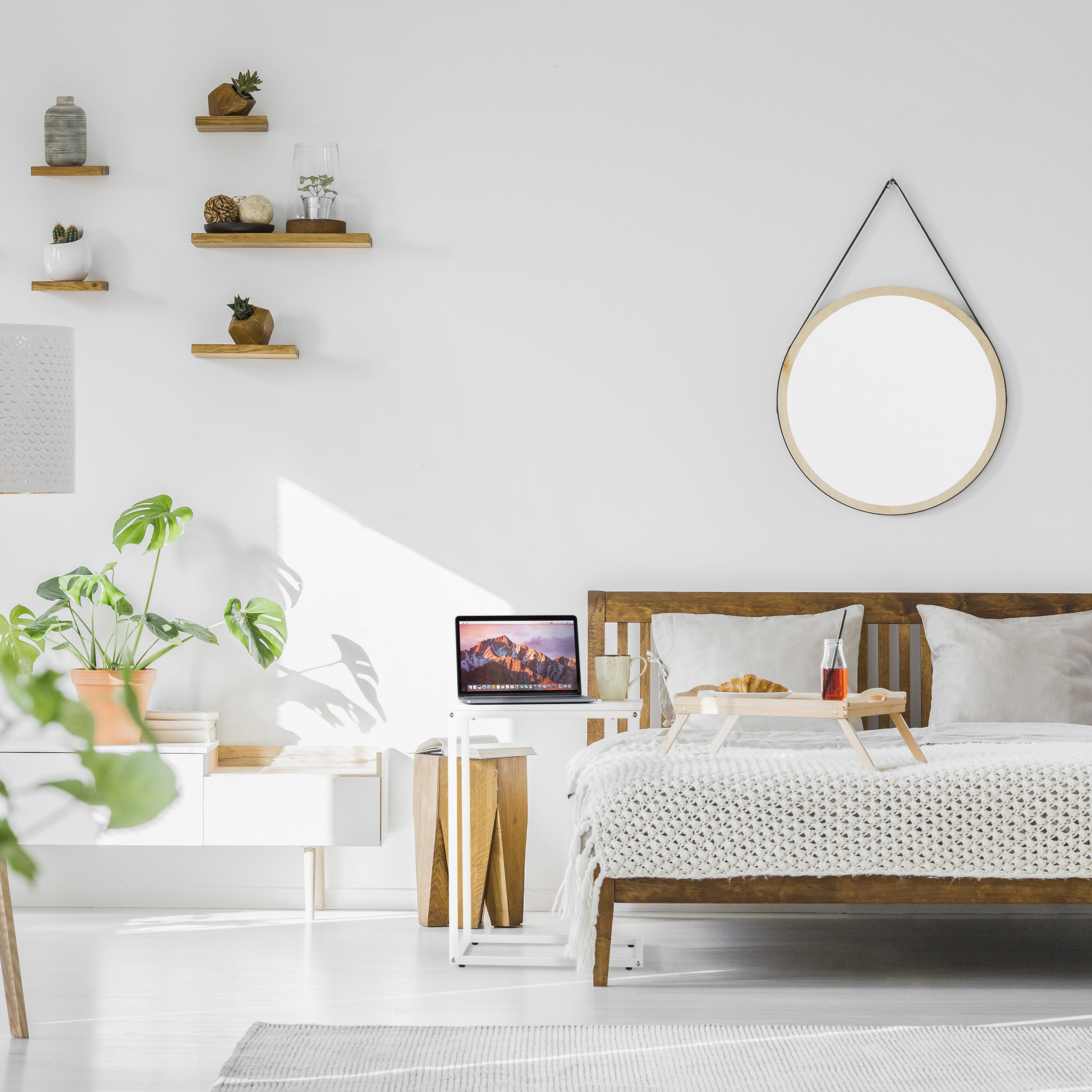 Gemütliches Schlafzimmer mit Holzbett, Laptop, runden Spiegel an der Wand und grünen Pflanzen.