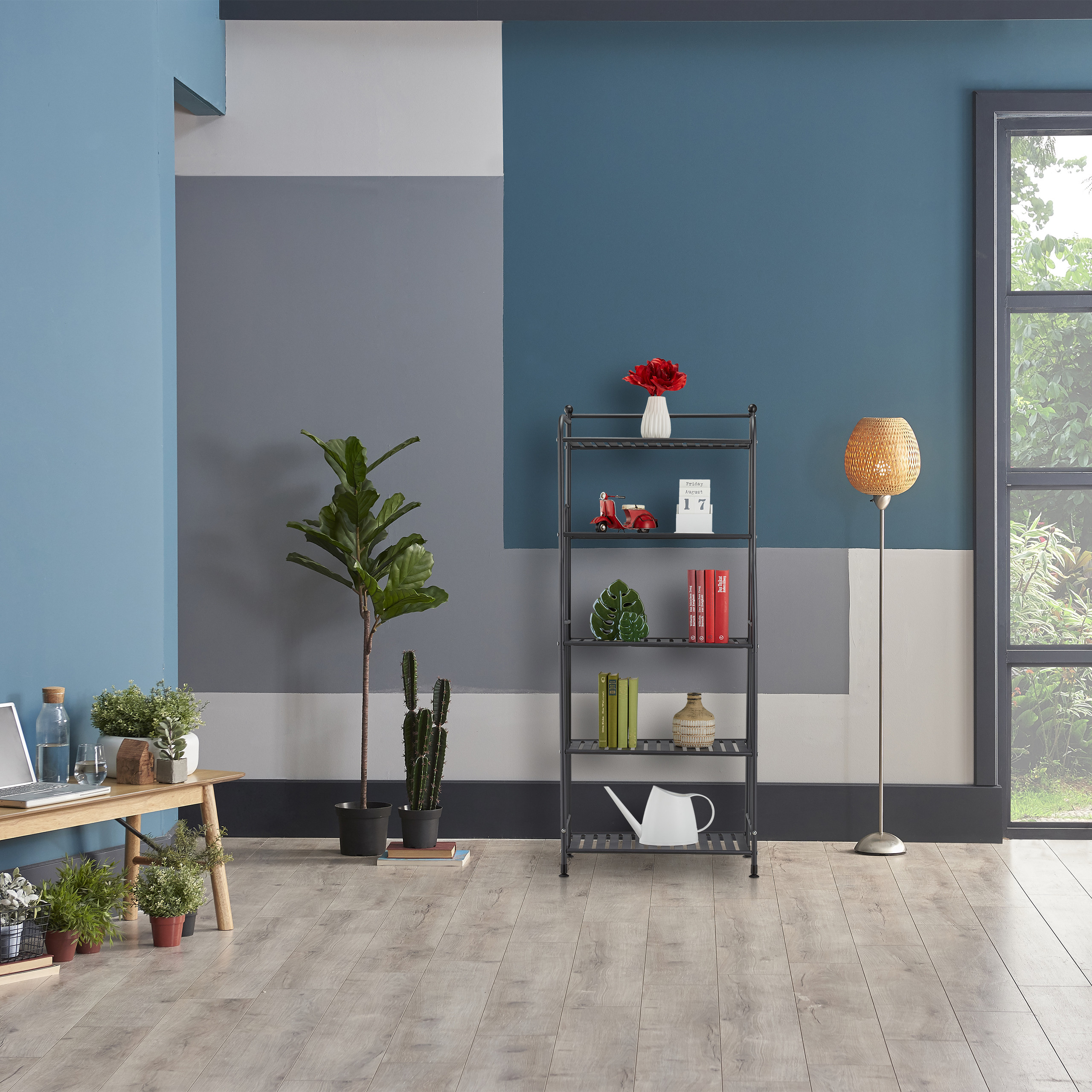 Moderne Inneneinrichtung mit blau-grauer Wand, Metallregal, Pflanzen, Lampe und Holztisch vor großem Fenster.