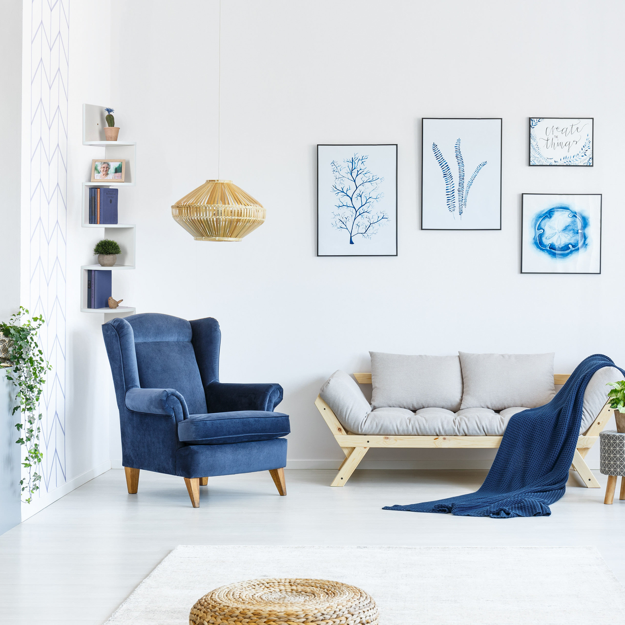 Wohnzimmer mit blauem Sessel, hellem Holzsofa mit grauen Kissen, blauer Decke und gerahmten Naturbildern.