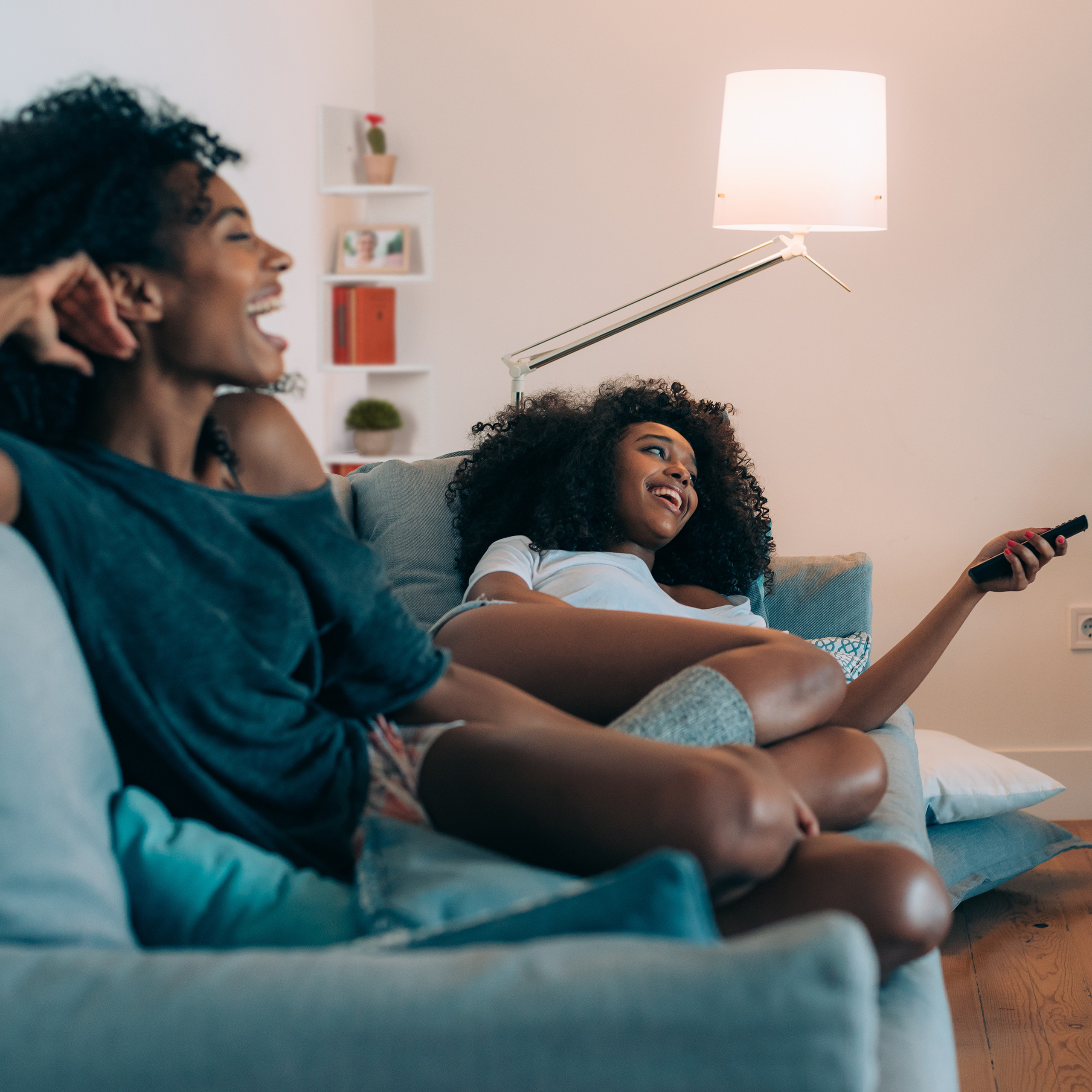 Zwei junge Frauen sitzen auf einem Sofa, lachen und schauen fern.