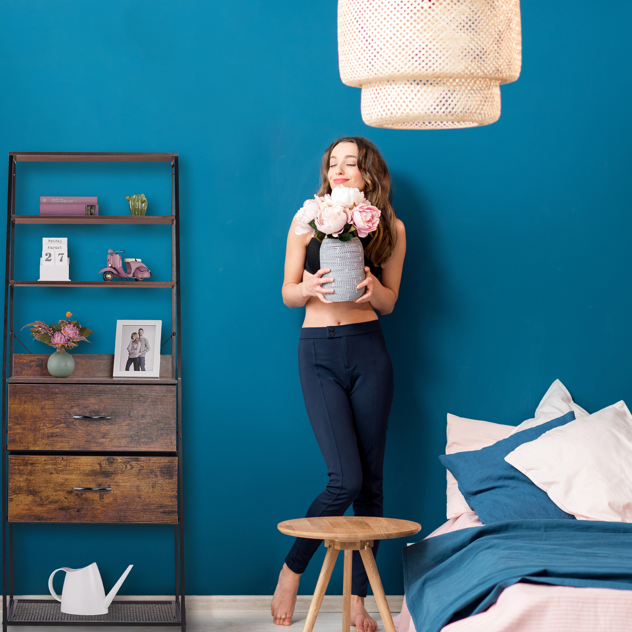 Frau mit geschlossenen Augen hält einen Blumenstrauß vor einer blauen Wand in einem Schlafzimmer.
