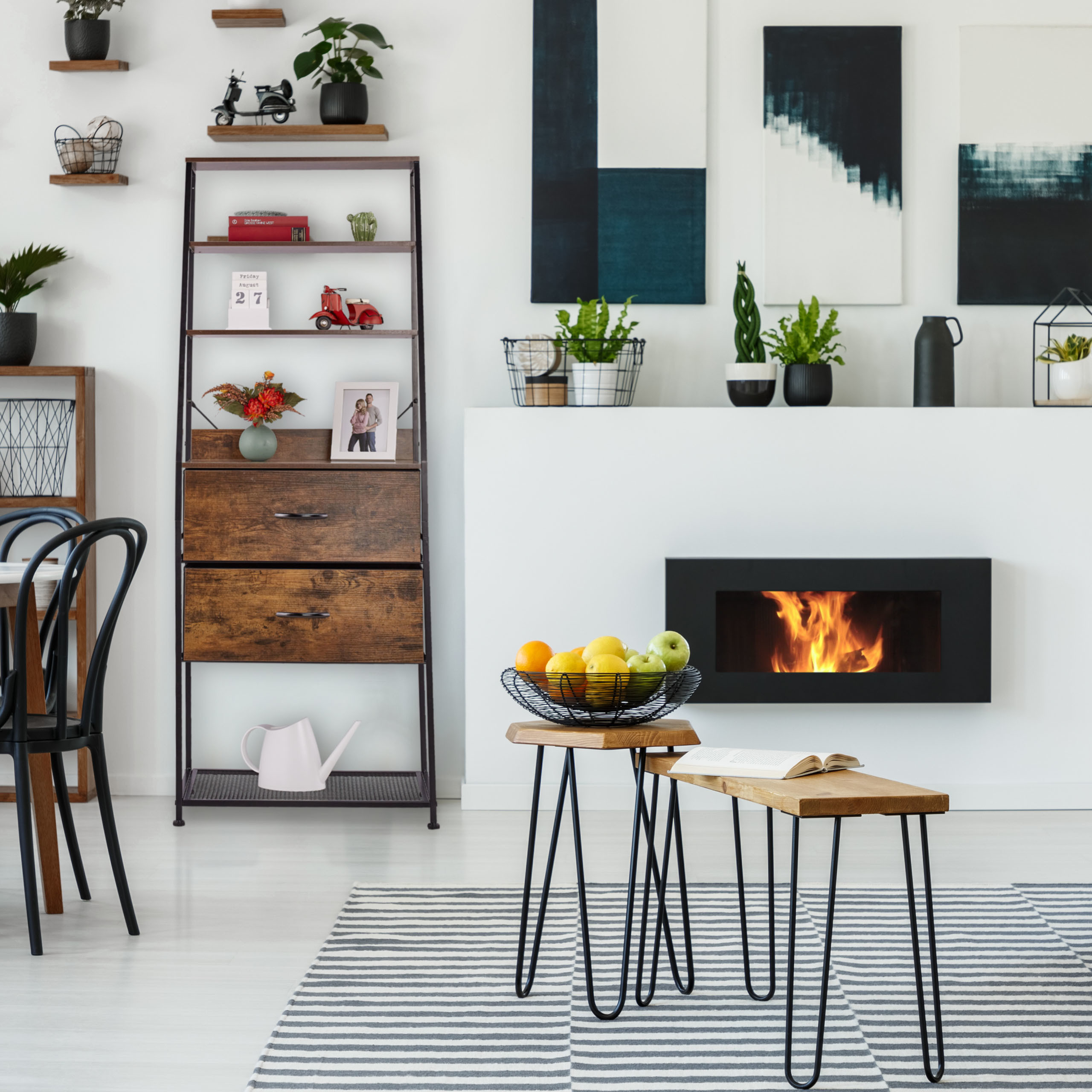 Gemütliches Wohnzimmer mit Kamin, Bücherregal und Holztischen mit Obstkorb auf einem gestreiften Teppich.