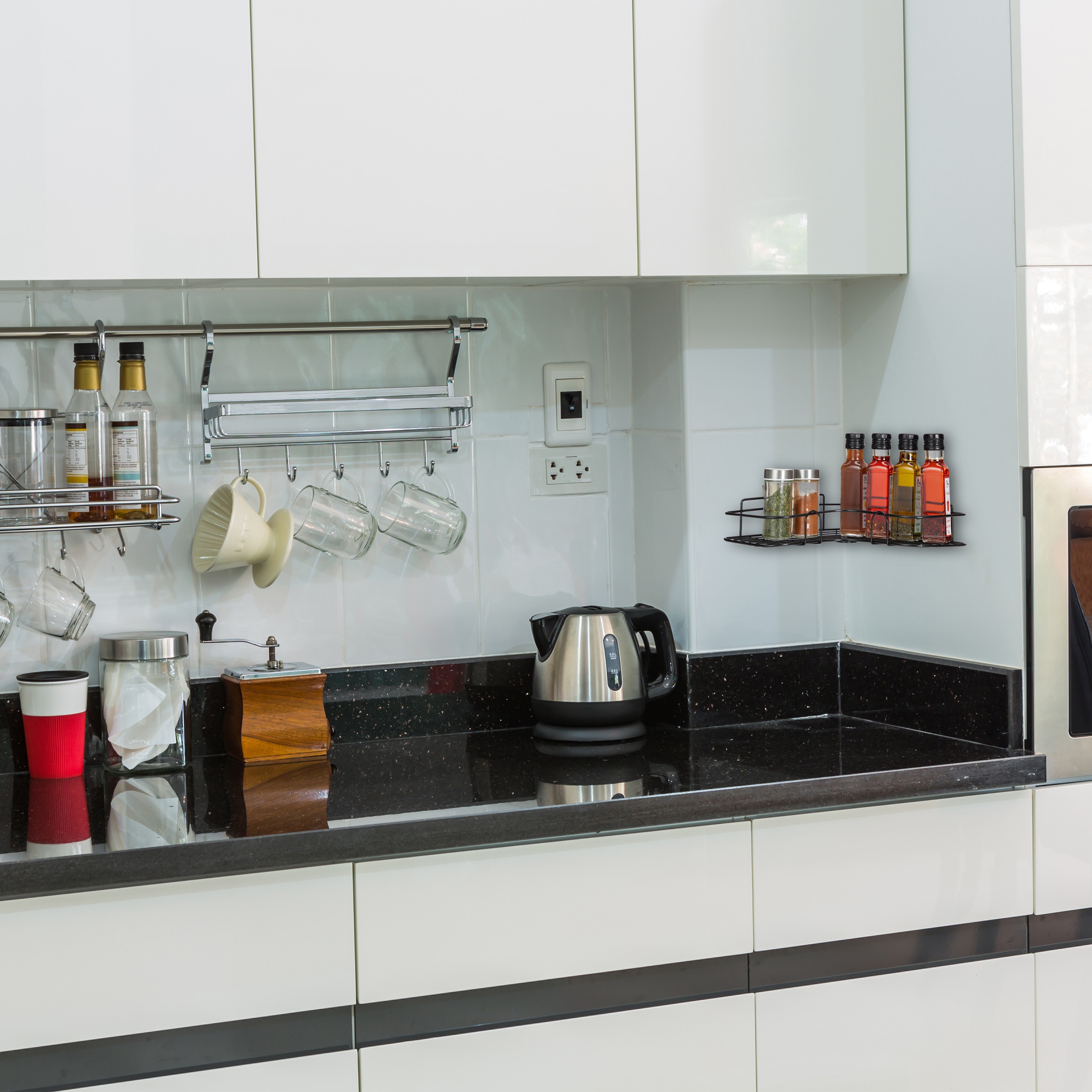 Weiße Küche mit schwarzer Granitarbeitsplatte, Kaffeemühle, elektrischem Wasserkocher und Gewürzregalen.
