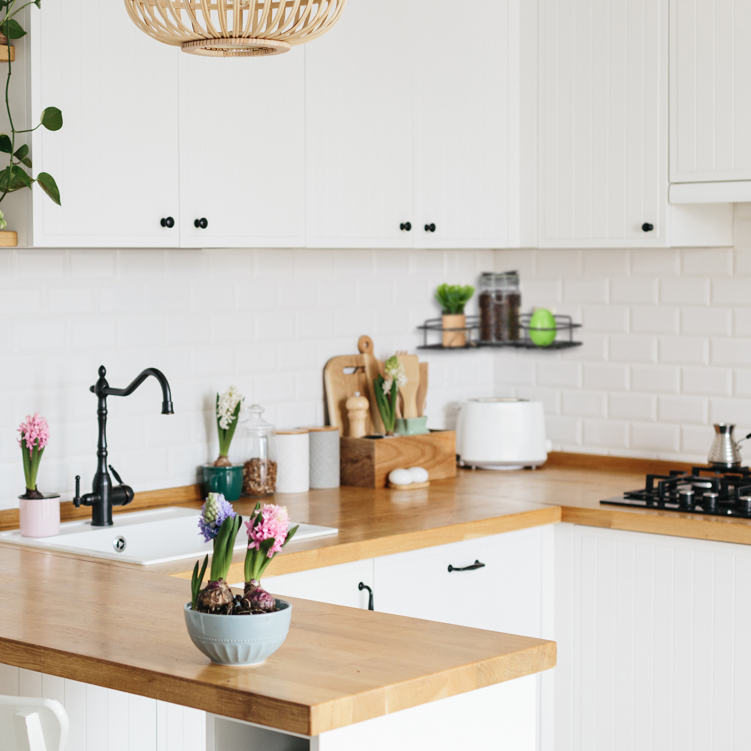 Helle, moderne Küche mit weißen Schränken, Holzarbeitsplatten, Topfblumen auf der Theke und einem schwarzen Wasserhahn.