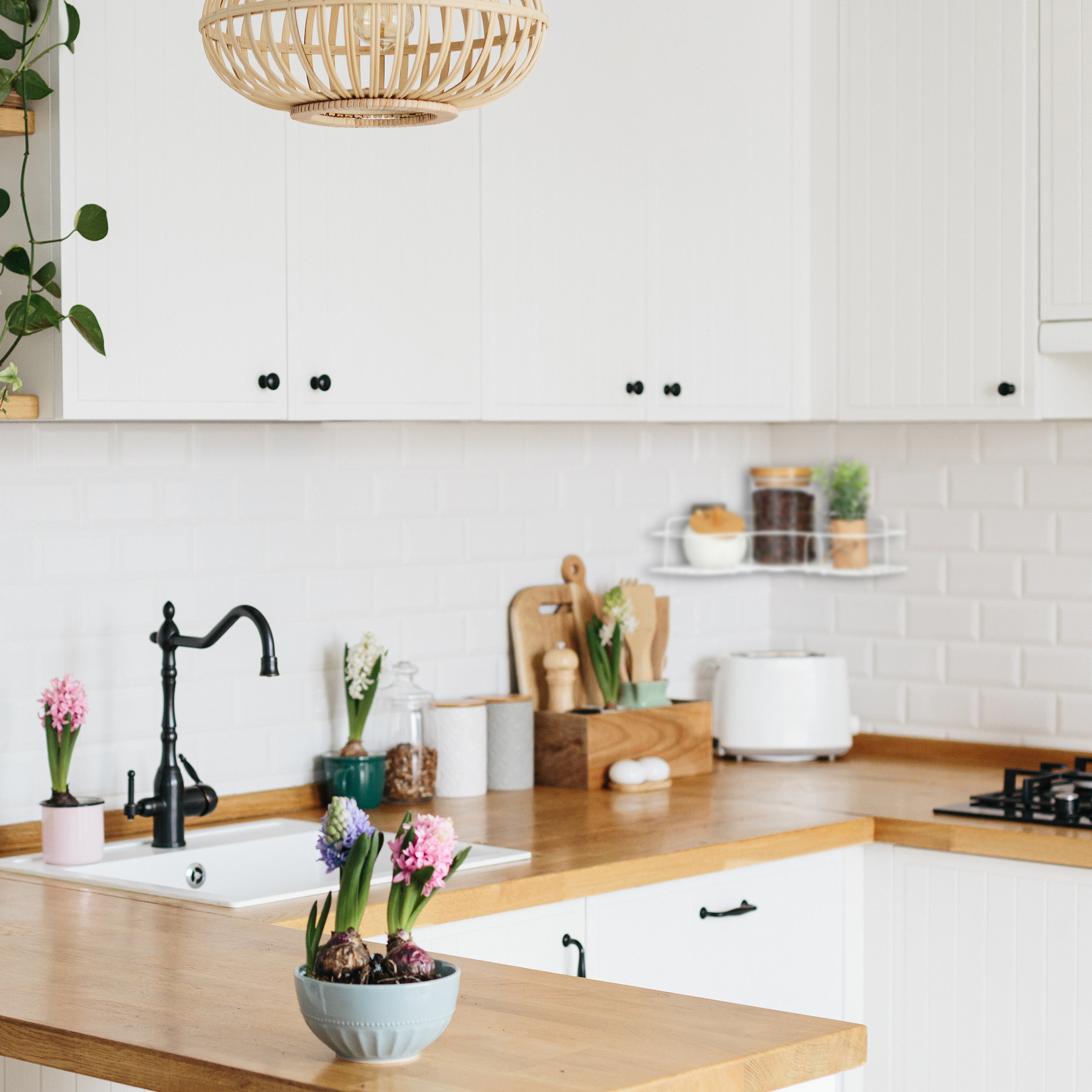Moderne weiße Küche mit Holzarbeitsplatte, Spüle, Blumen im Topf und einer Korblampe an der Decke.