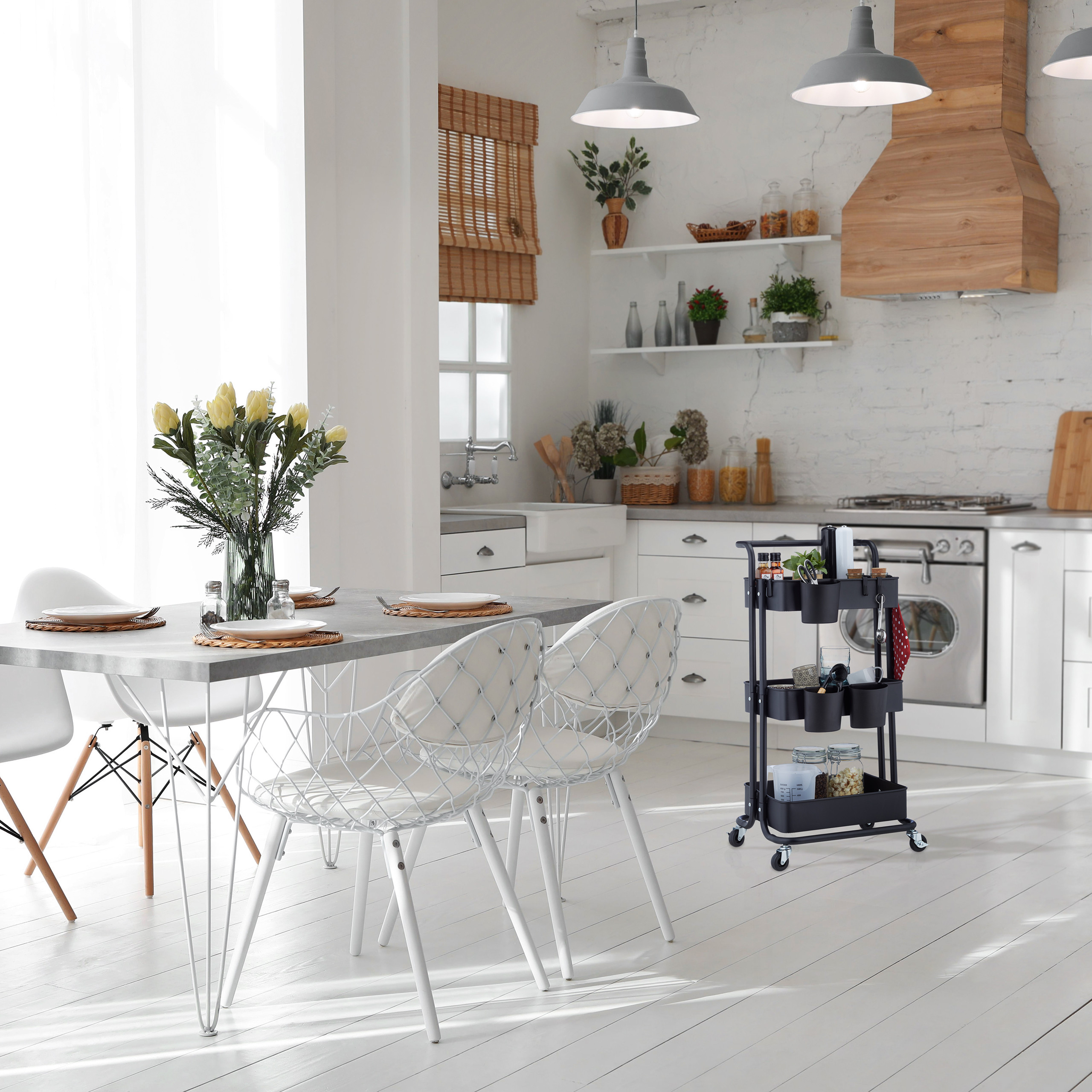 Helle Küche mit Esstisch, weißen Stühlen, gelben Blumen und einem schwarzen Servierwagen.
