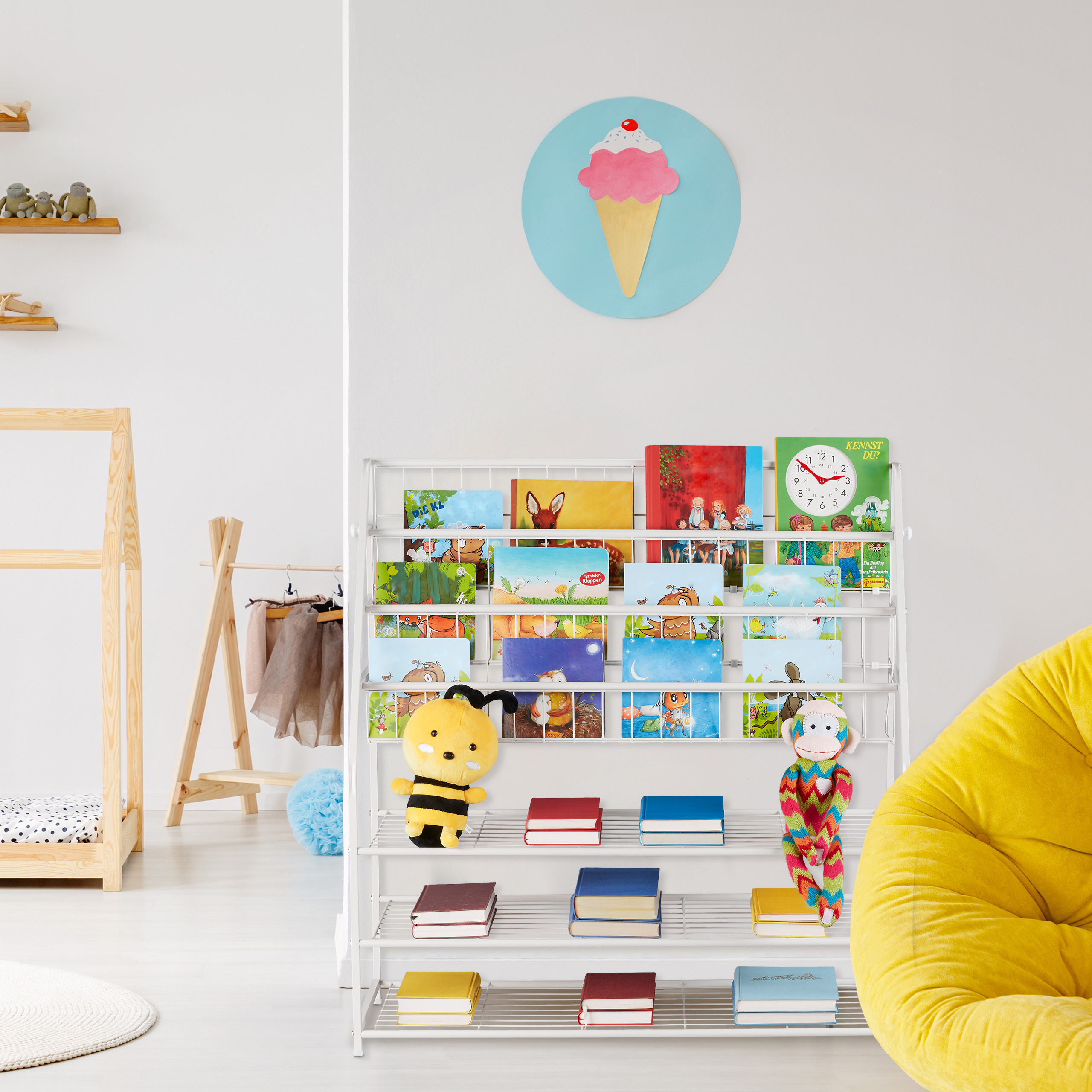 Bücherregal in einem Kinderzimmer mit farbigen Büchern, Spielzeug, Wanduhr mit Eiscrememotiv und gelbem Sitzsack.