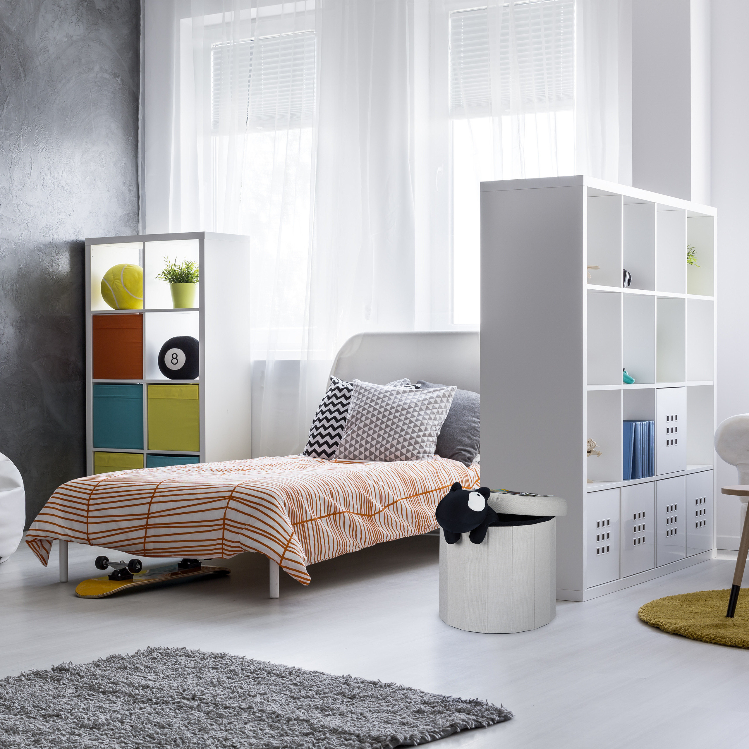 Ein modernes Kinderzimmer mit einem Bett mit orange-weißer Bettwäsche, weißen Regalen und einem Skateboard.
