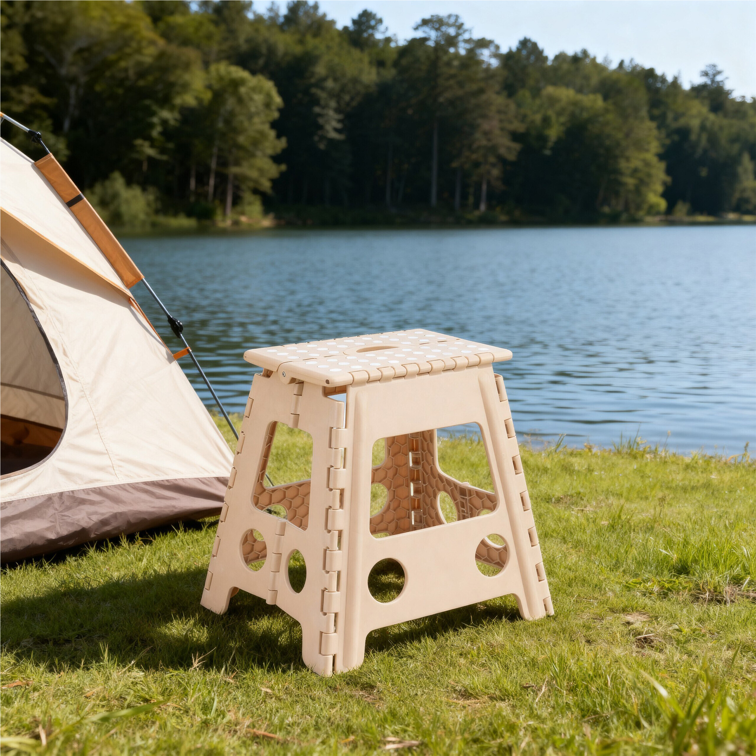 Ein beiger Klapphocker auf der Wiese neben einem Zelt, im Hintergrund ein See und Wald.