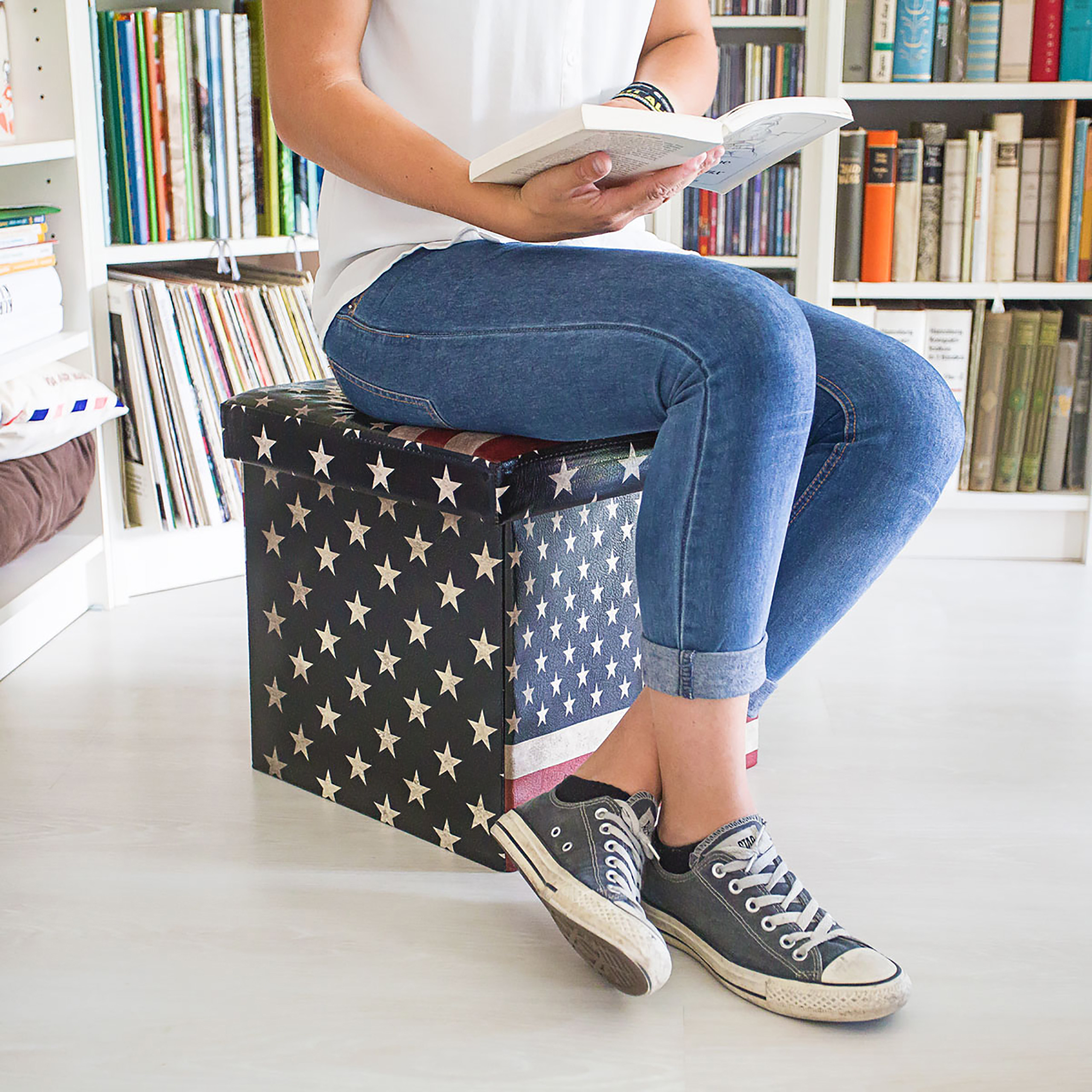 Eine Person liest ein Buch auf einer US-Flaggen-Sitzkiste in einem Zimmer mit Bücherregalen.