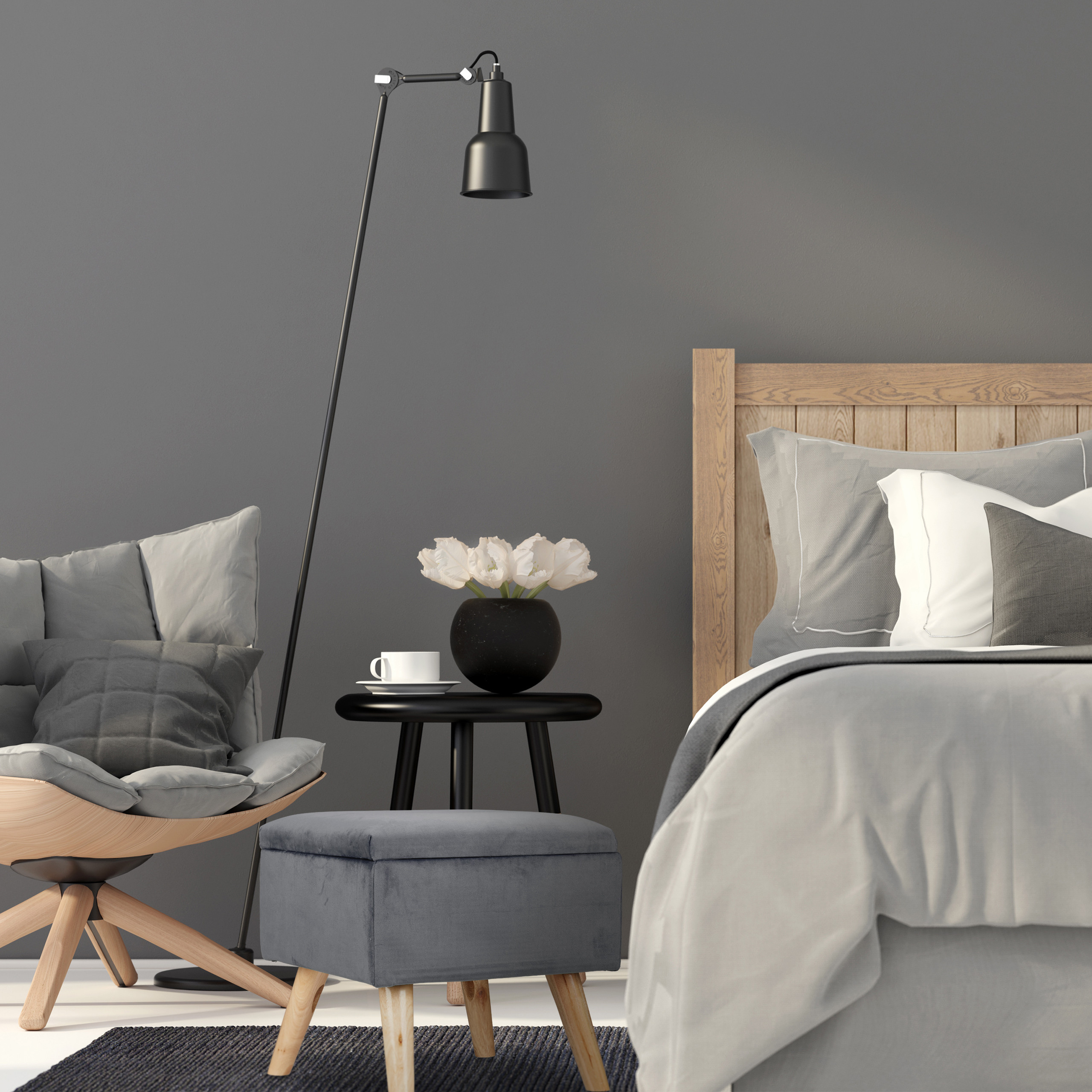 Moderne Schlafzimmerecke mit grauem Sessel, passendem Hocker, Nachttisch mit Blumen und Stehlampe vor grauer Wand.