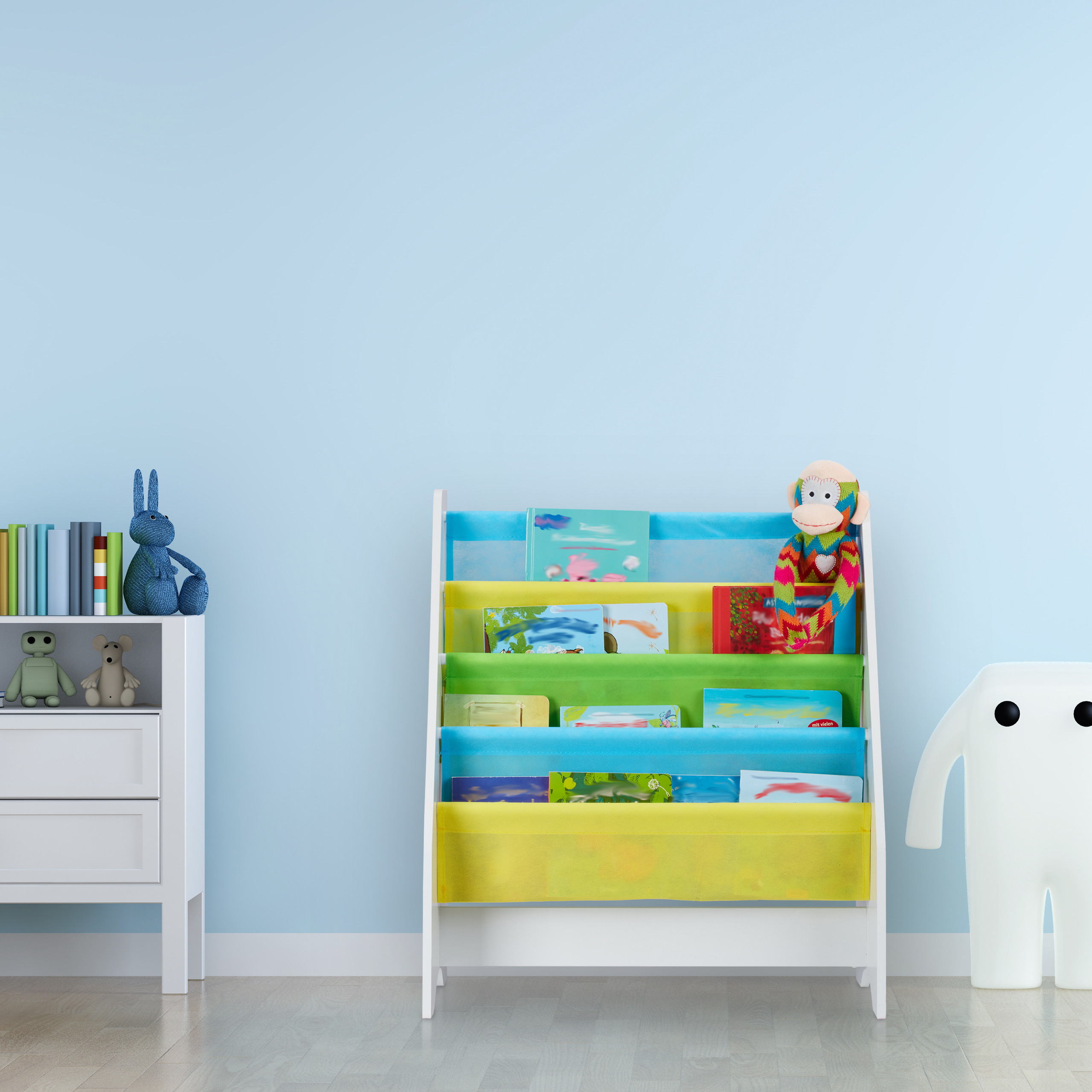 Ein buntes Kinderregal mit Büchern und einem Plüschaffen, neben einem weißen Schrank und einer Figurenlampe an einer blauen Wand.