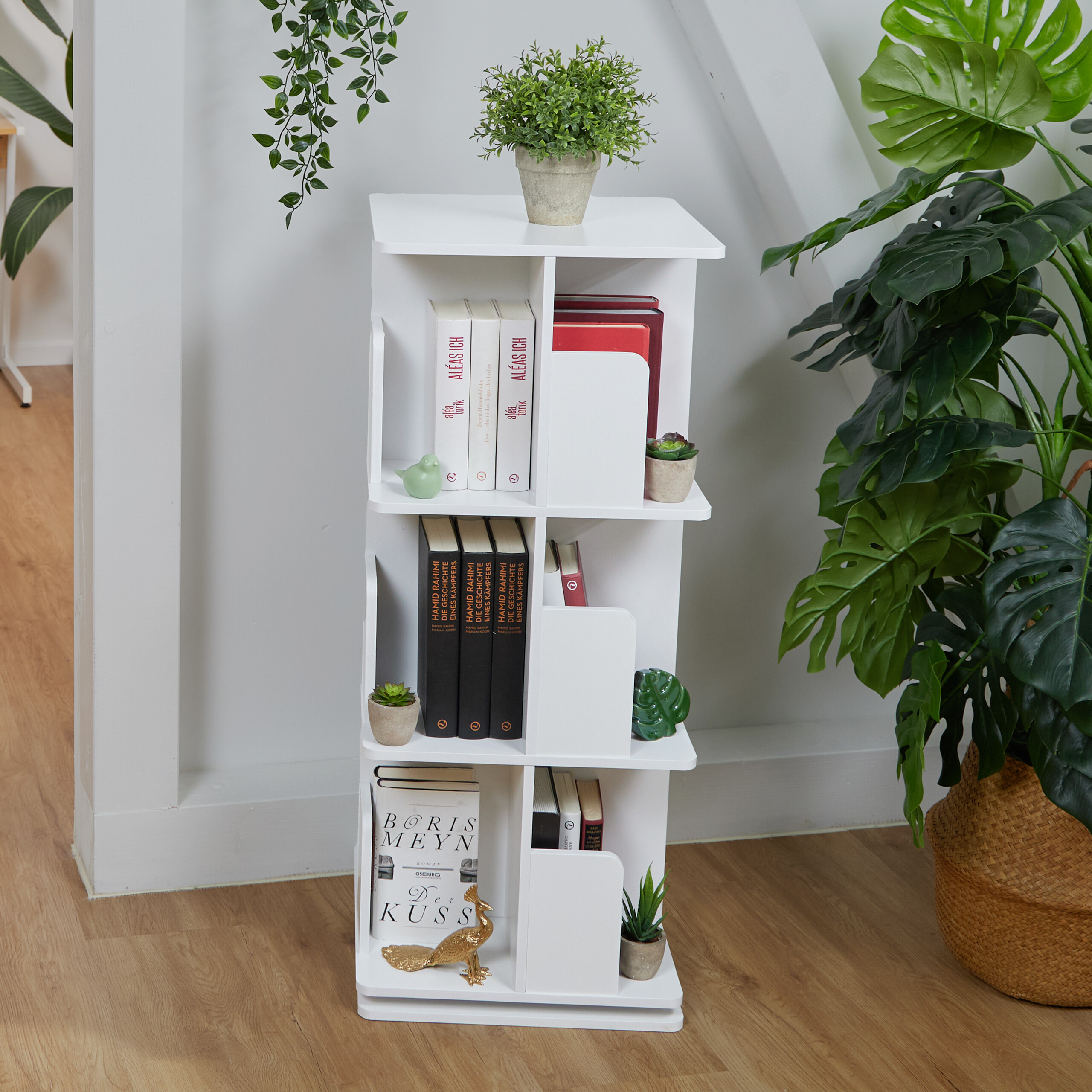 Ein weißes Bücherregal mit verschiedenen Büchern und dekorativen Pflanzen, flankiert von großen grünen Zimmerpflanzen.