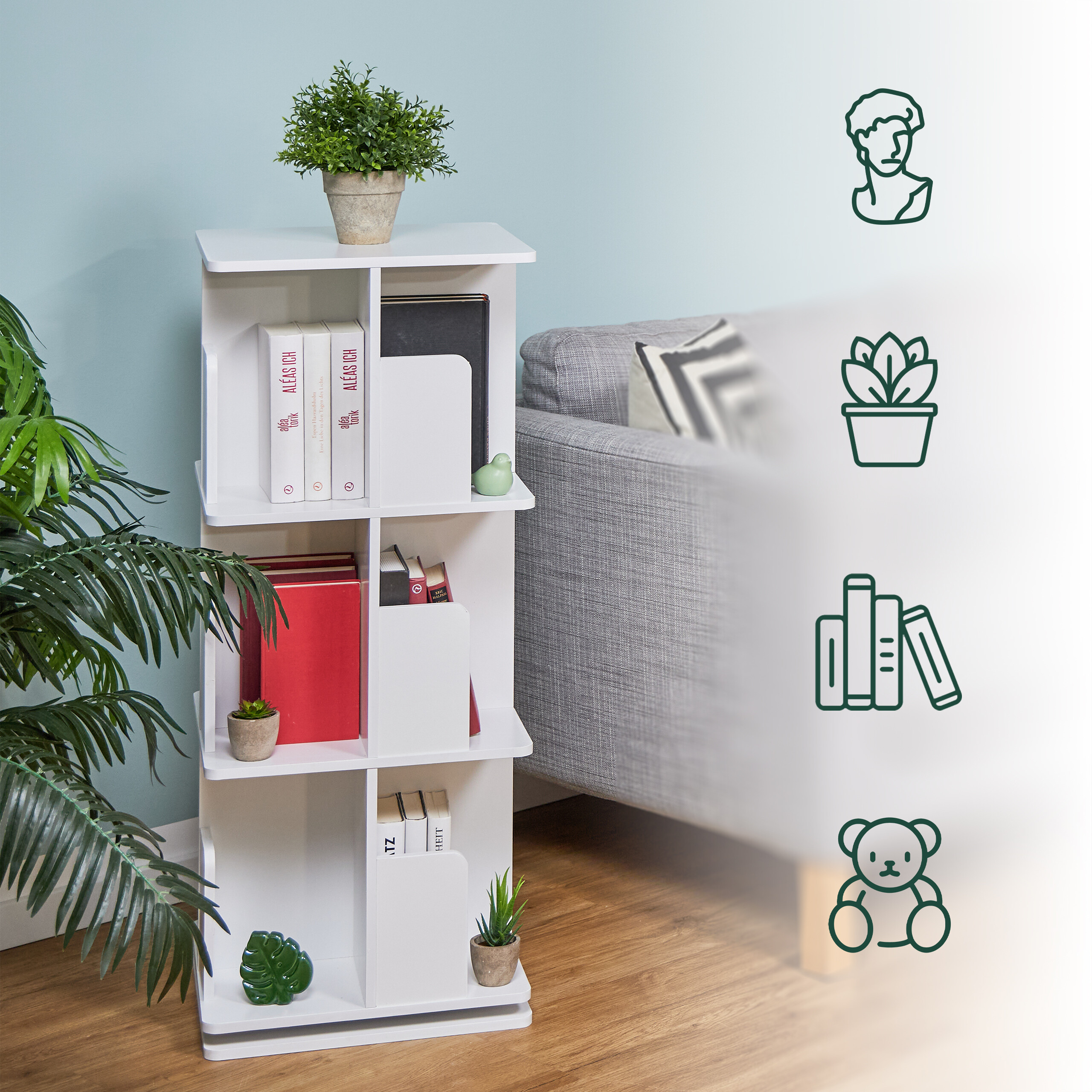 Ein drehbares weißes Regal mit Büchern, Pflanzen und einem grauen Sofa im Hintergrund.