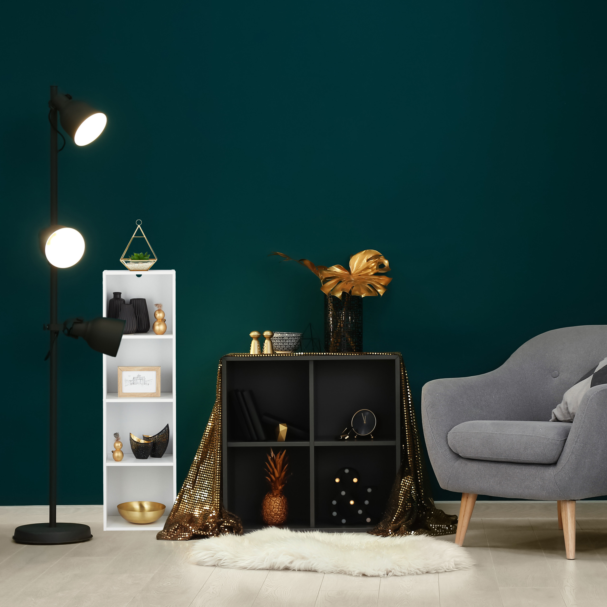 Ein gemütliches Zimmer mit dunklen Wänden, einem grauen Sessel, Regalen mit Deko und einer goldenen Tischdecke.