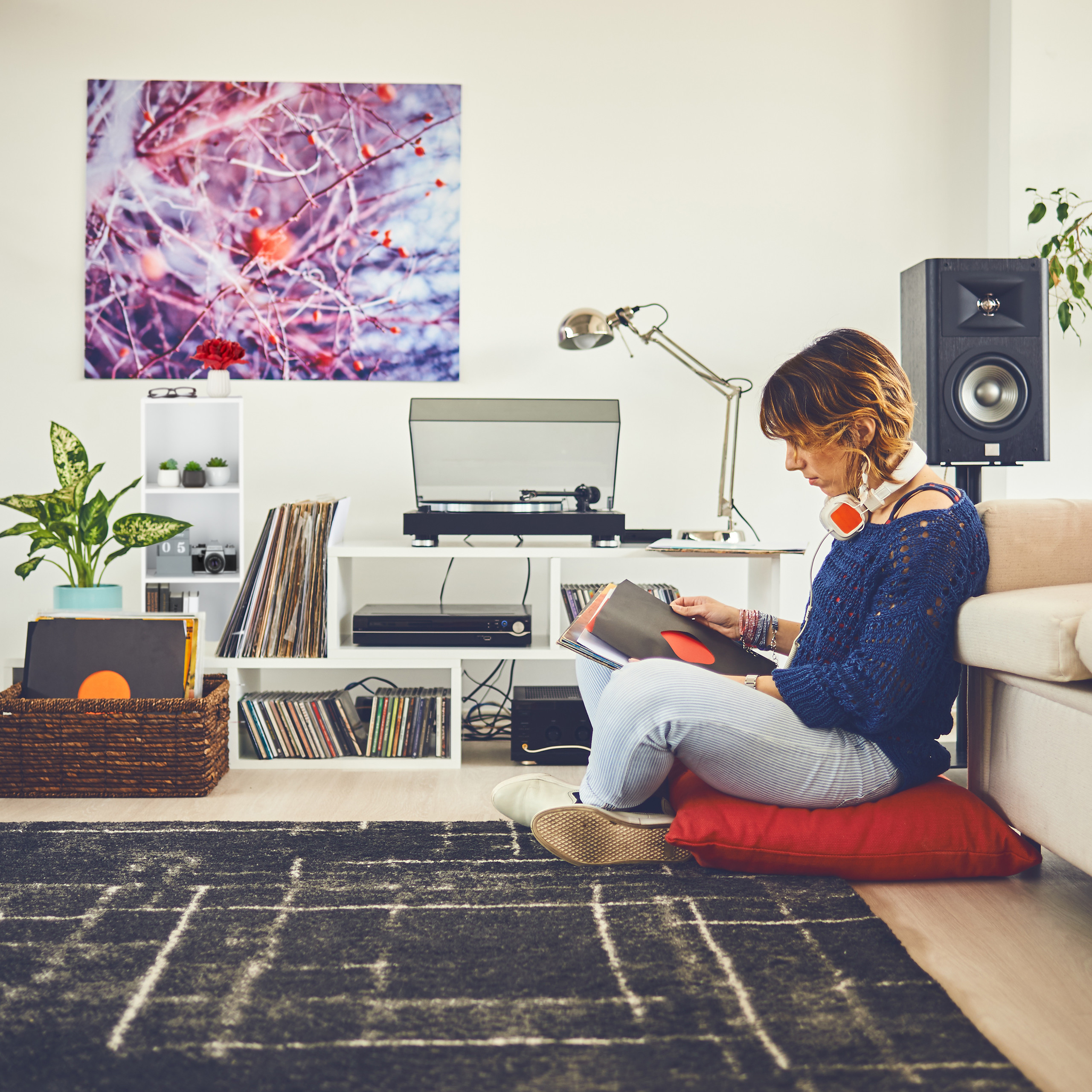 Eine Frau sitzt auf einem roten Kissen auf dem Boden und stöbert in einem Wohnzimmer in Schallplatten.