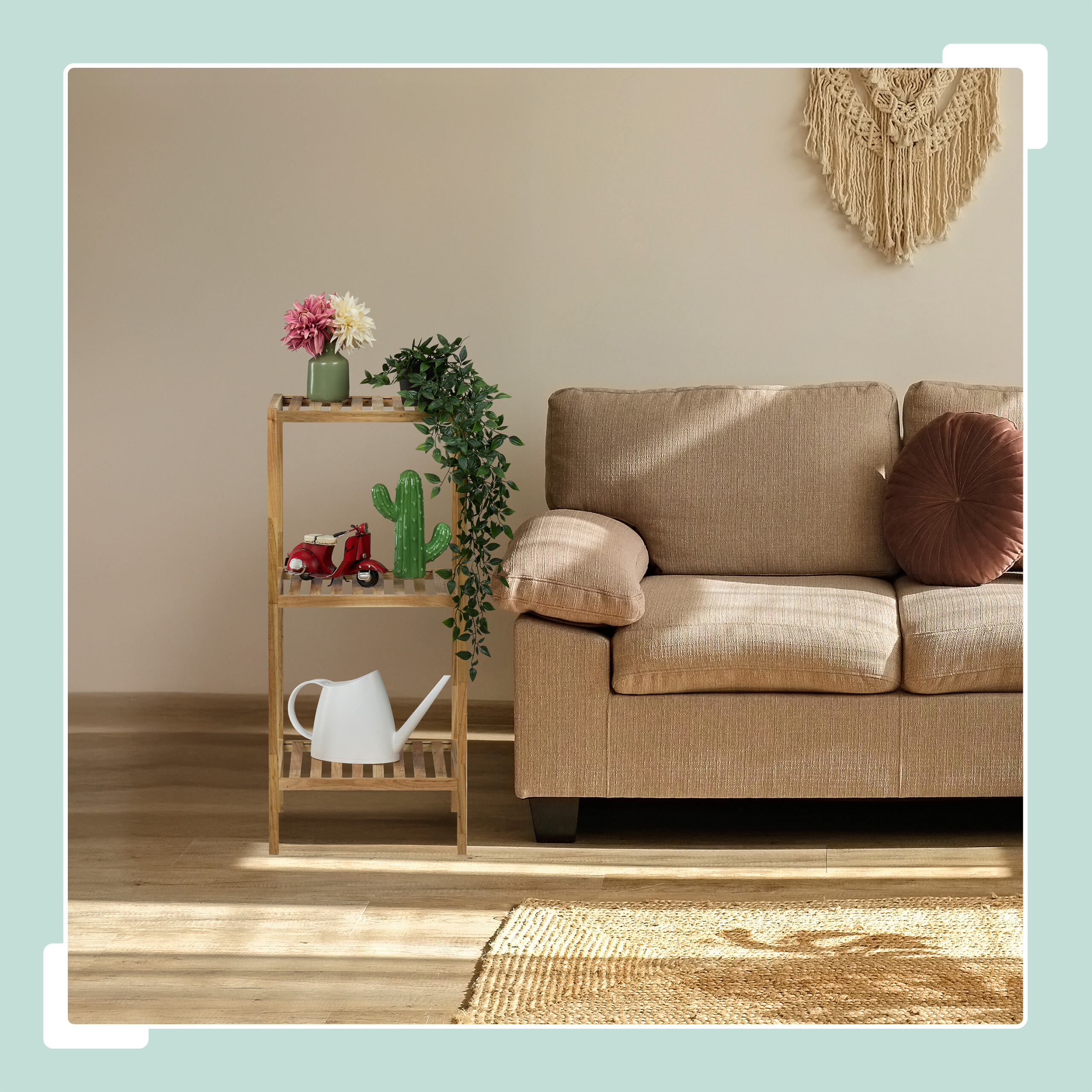 Ein Wohnzimmer mit beigem Sofa, Holzregal mit Blumen, Kaktus und Gießkanne, Makramee an der Wand.