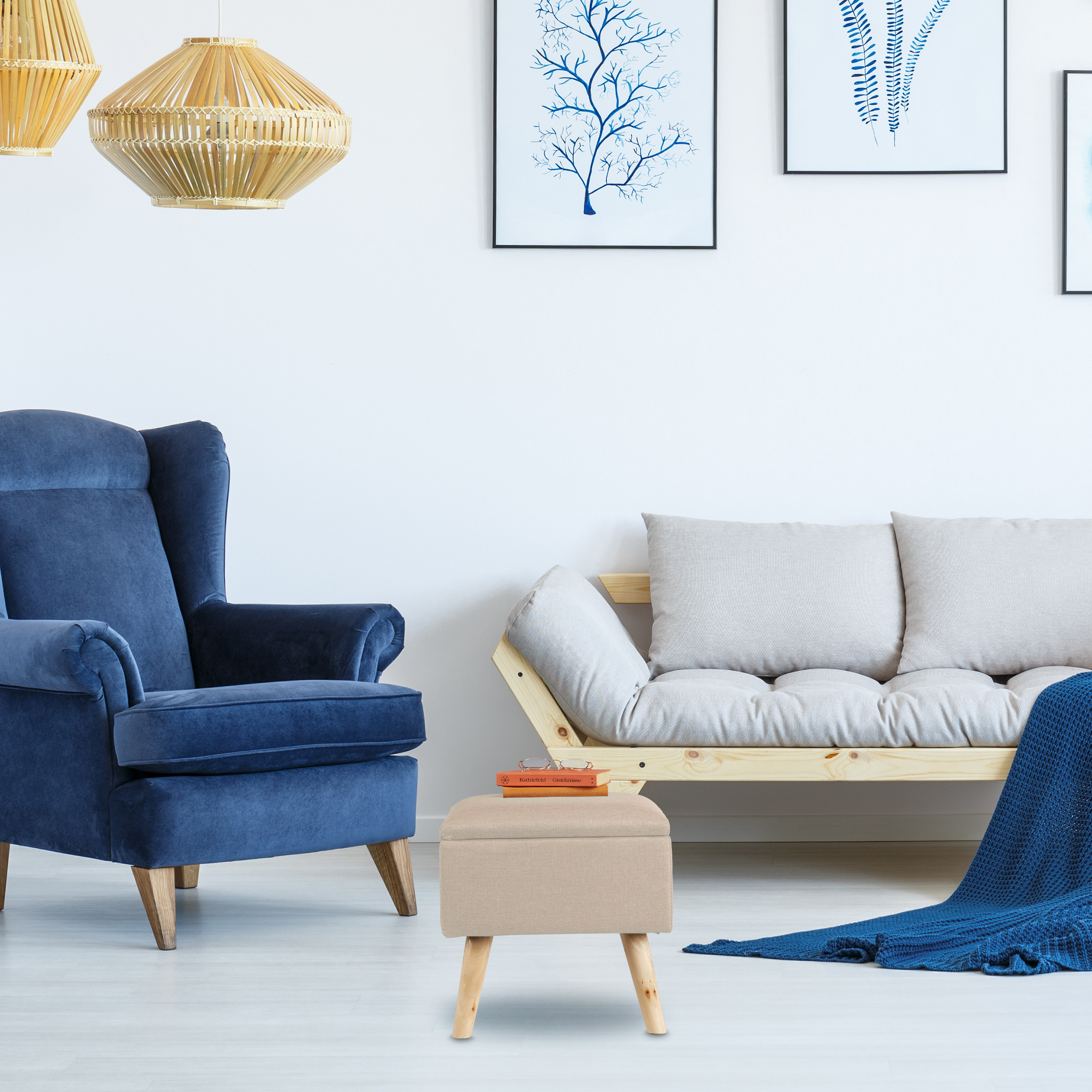 Wohnzimmer mit blauem Sessel, beigem Sofa, Hocker und blauen Hängelampen vor weißer Wand mit Kunst.