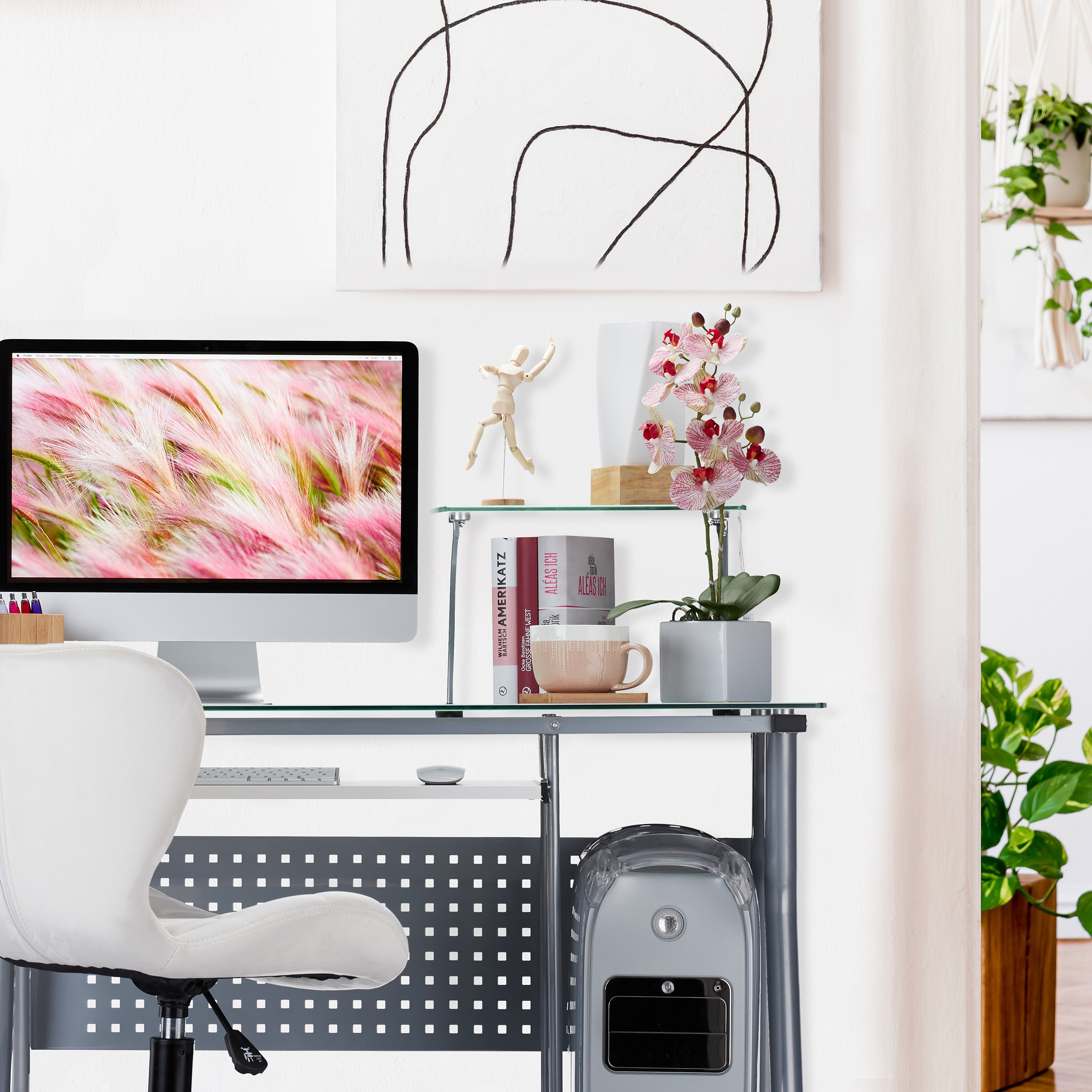 Moderner Schreibtisch mit Computer, Regal mit Orchidee, Holzmännchen und Büchern vor weißer Wand.