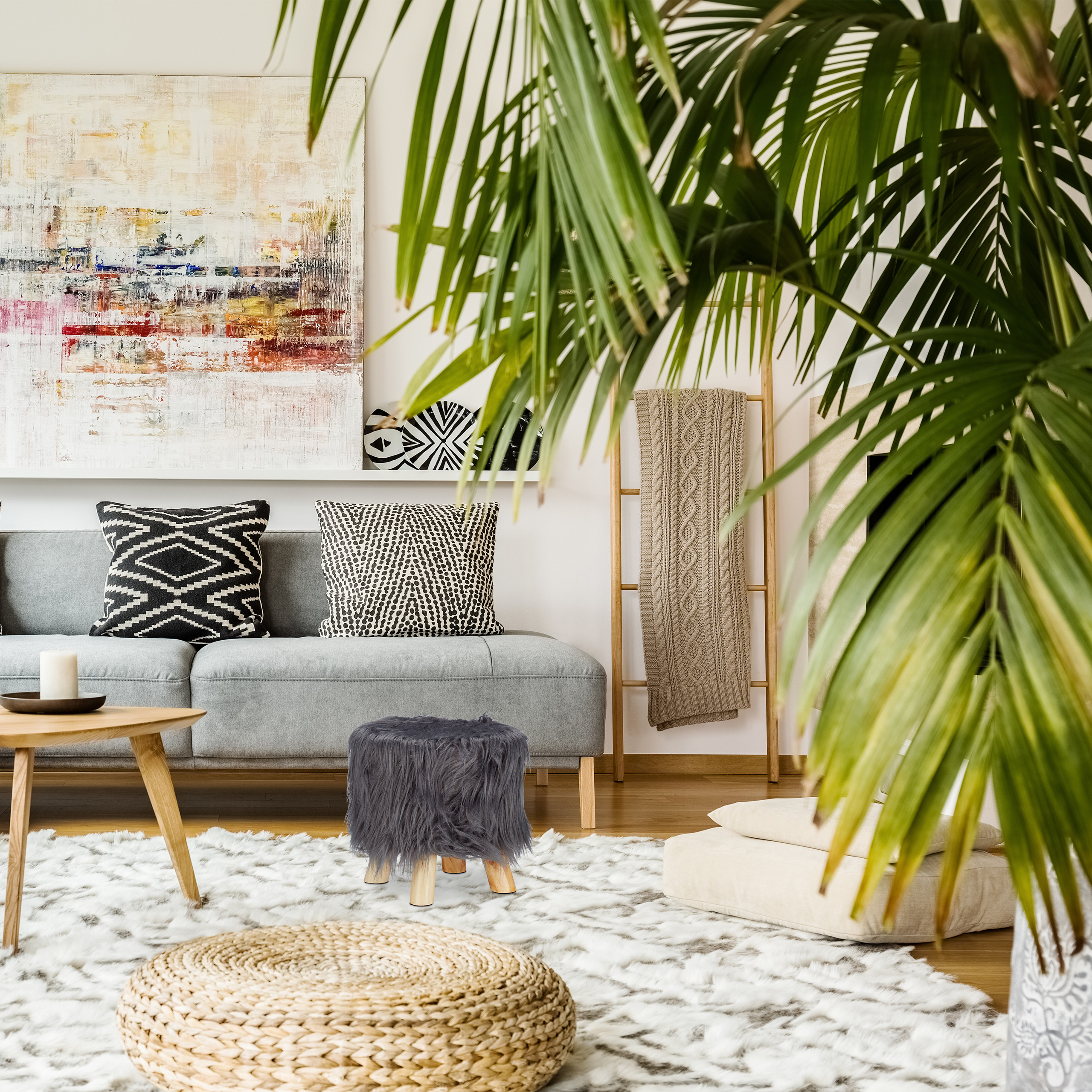 Wohnzimmer mit grauem Sofa, gemusterten Kissen, großem Kunstwerk, Teppich und Palmenpflanze im Vordergrund.
