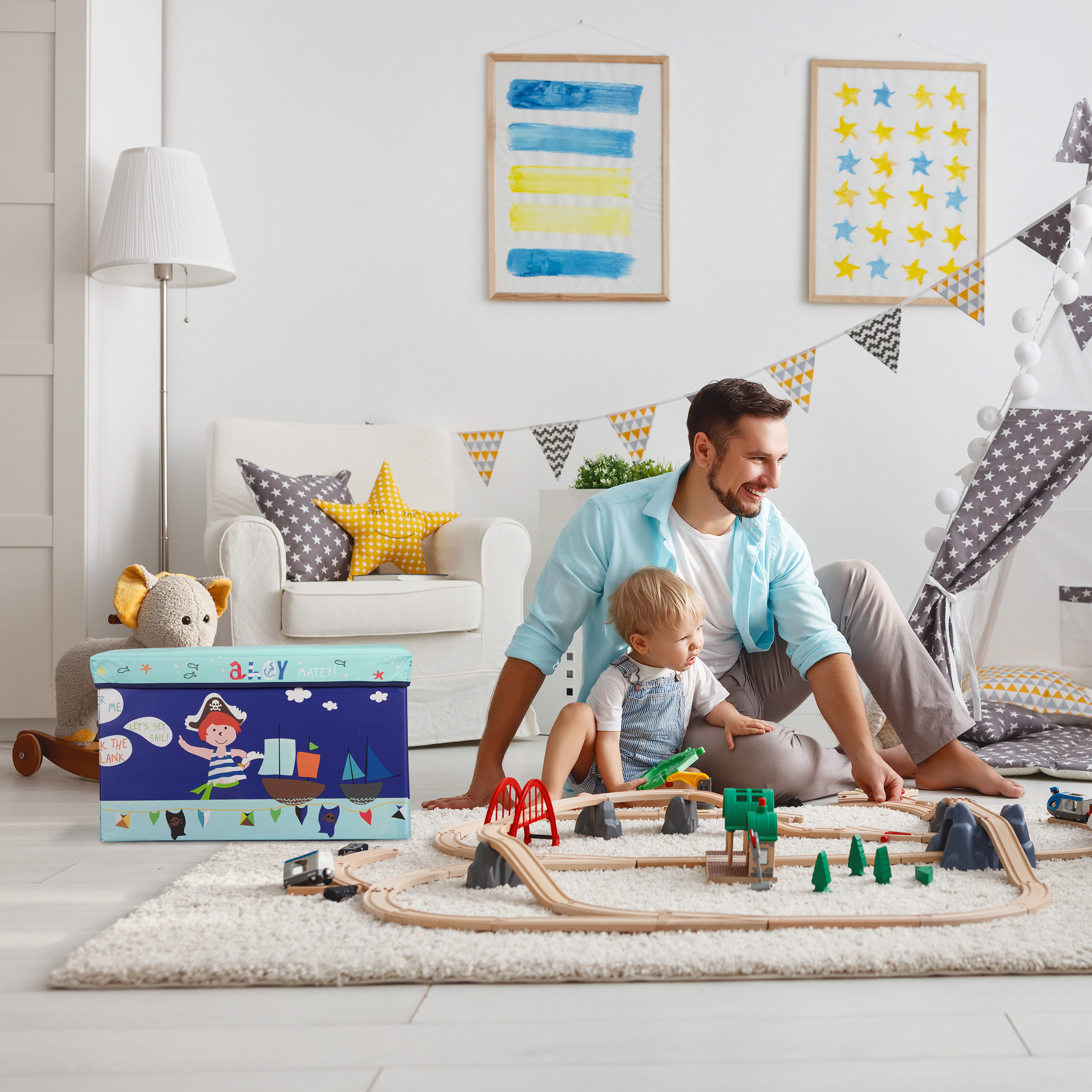 Ein Vater und sein kleiner Sohn spielen im hellen Kinderzimmer mit einer Holzeisenbahn auf dem Teppich.