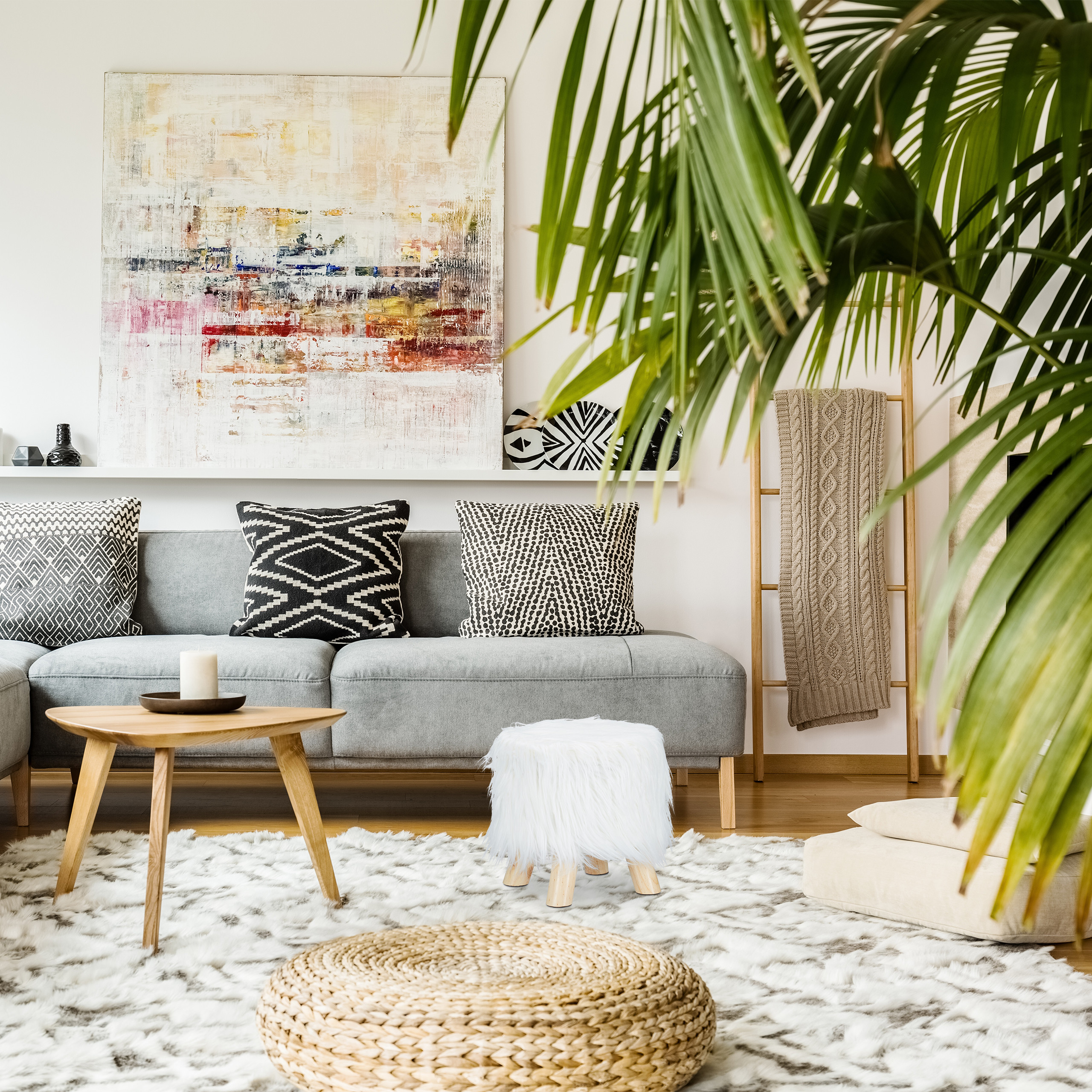 Ein graues Sofa mit Kissen, Holztisch und großem abstrakten Gemälde in einem hellen Wohnzimmer.