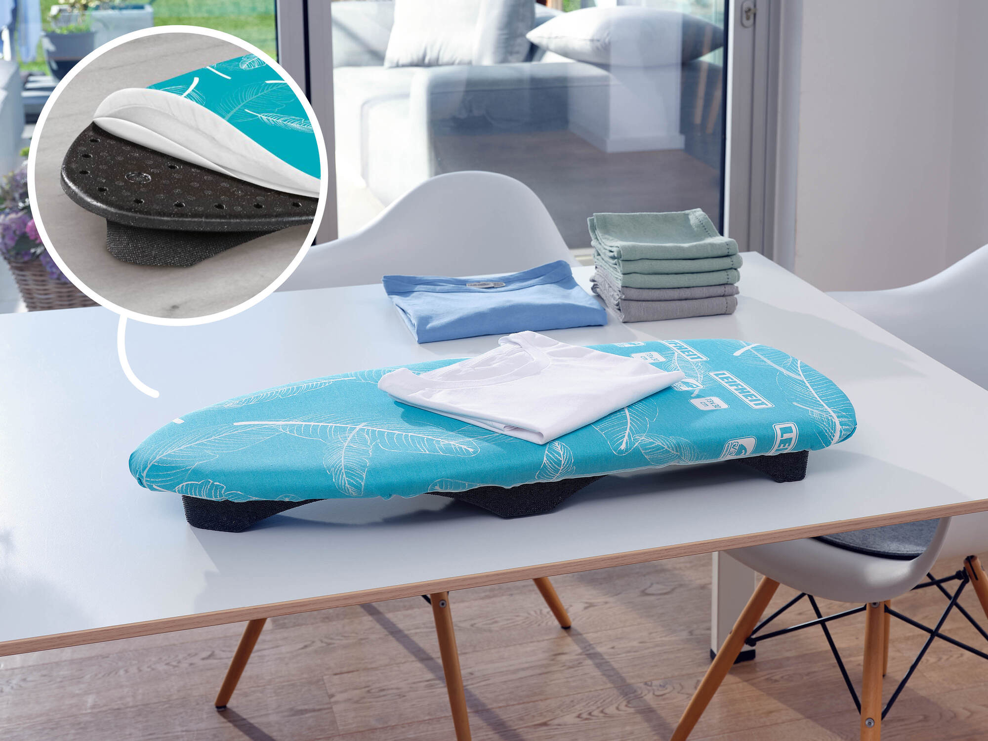 Ein kleines blaues Bügelbrett mit einem weißen T-Shirt darauf steht auf einem Tisch, mit einem Schichtdetails-Inset.