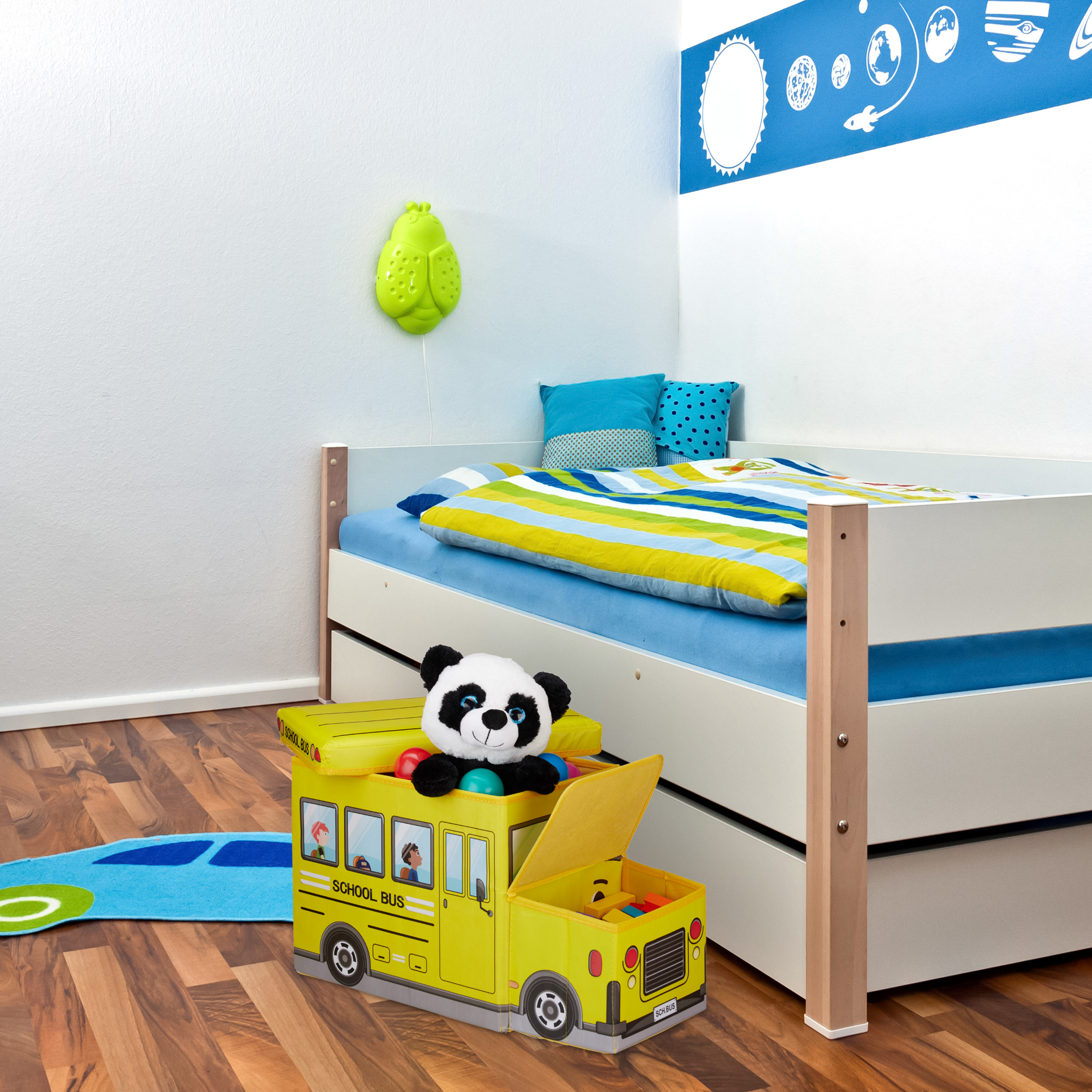 Kinderzimmer mit weißem Bett, blauer Bettwäsche, gelber Spielzeugkiste als Schulbus und Panda-Stofftier.