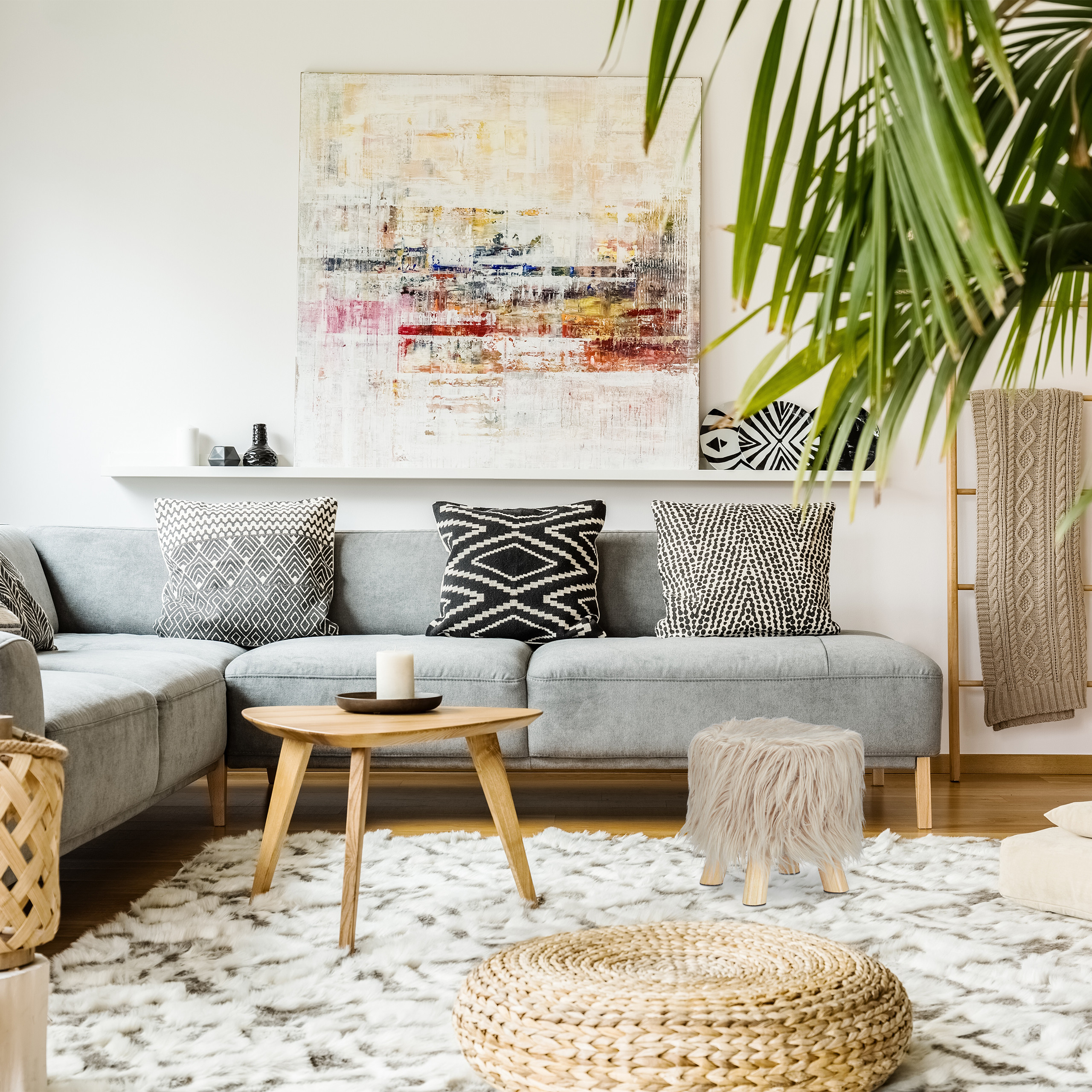 Gemütliches Wohnzimmer mit grauem Sofa, gemusterten Kissen, abstrakter Kunst und einer grünen Pflanze im Vordergrund.