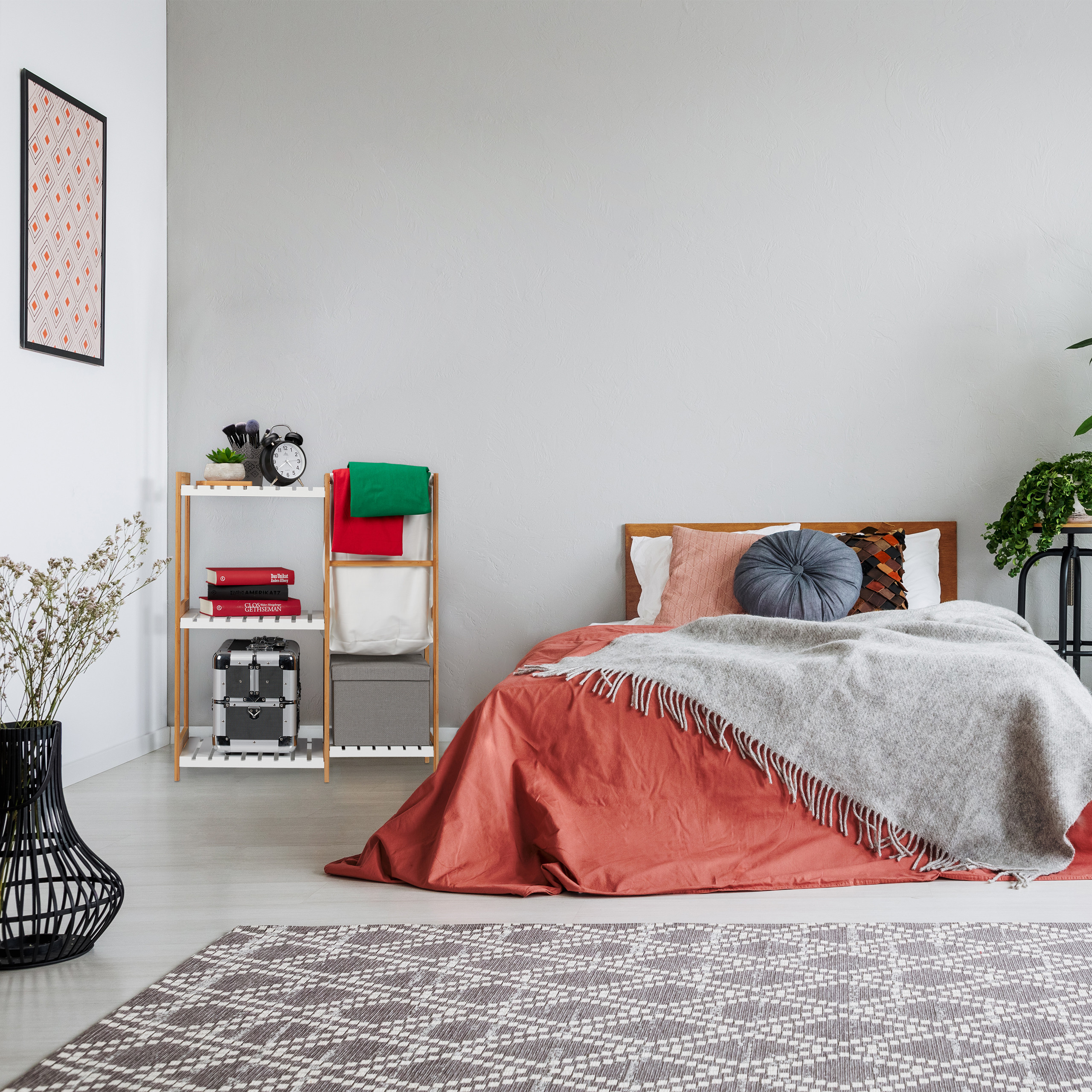 Gemütliches Schlafzimmer mit roter Bettwäsche, grauer Decke, Holzbett, Regalen und gemustertem Teppich.