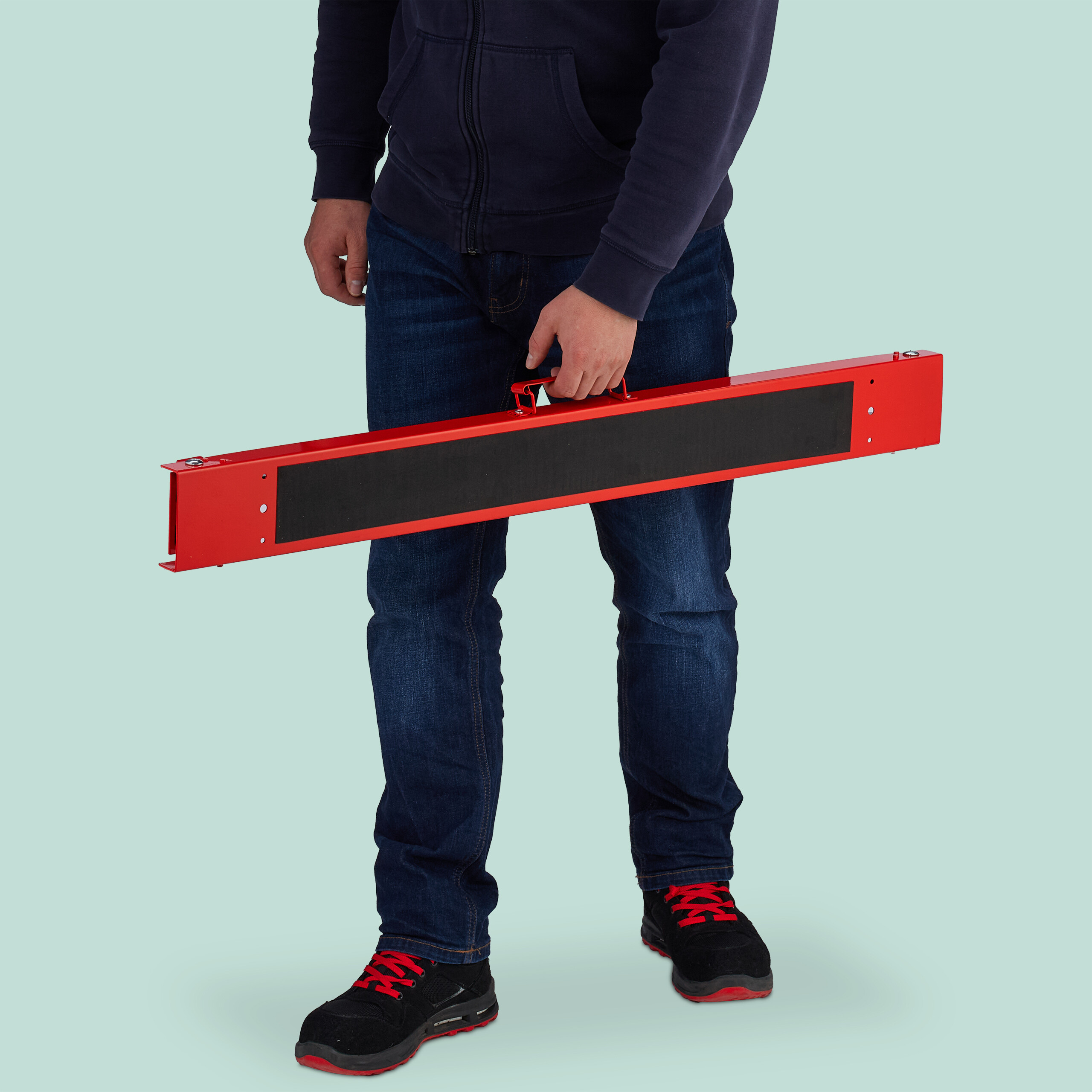 Mann in Jeans und blauem Hoodie hält eine lange rote Stange mit schwarzer Einlage.