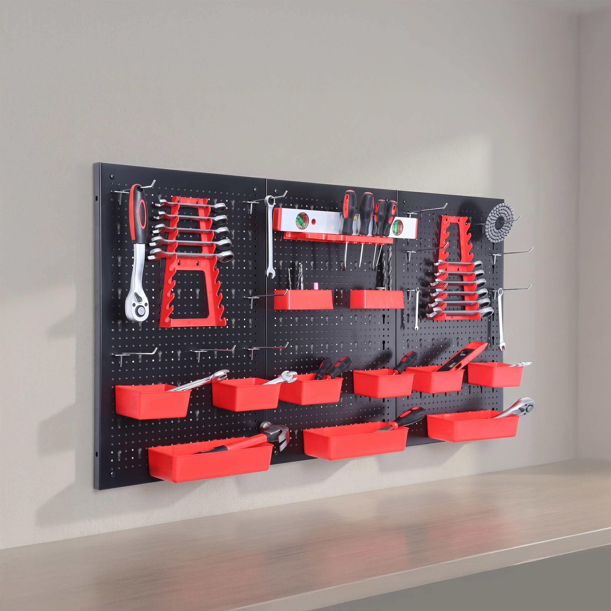 Eine schwarze Lochwand mit roten Werkzeughaltern und -kästen hängt an einer grauen Wand über einer Ablage.