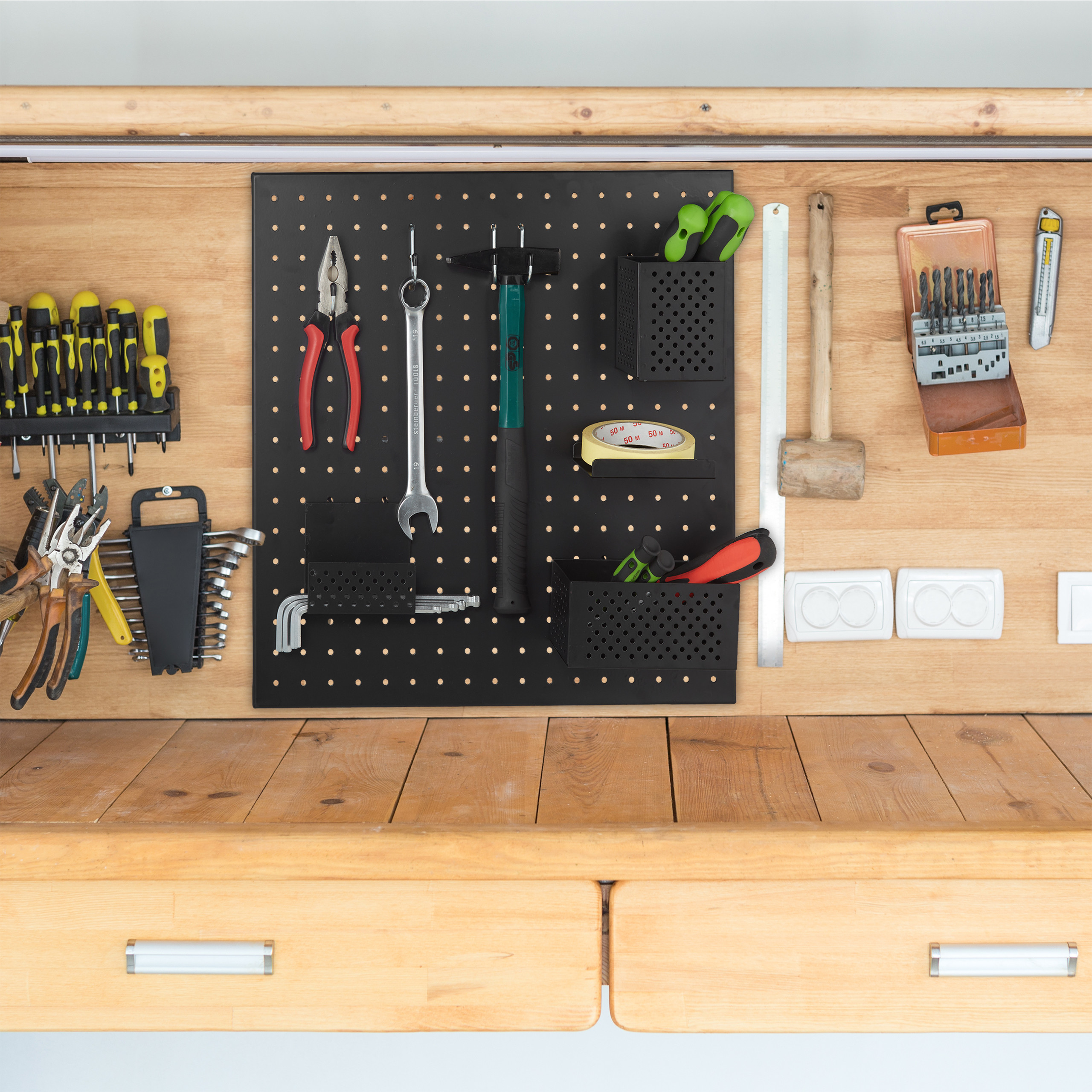 Eine Holzwerkbank mit Werkzeugen, die ordentlich auf einer schwarzen Lochwand und an der Wand darüber angeordnet sind.