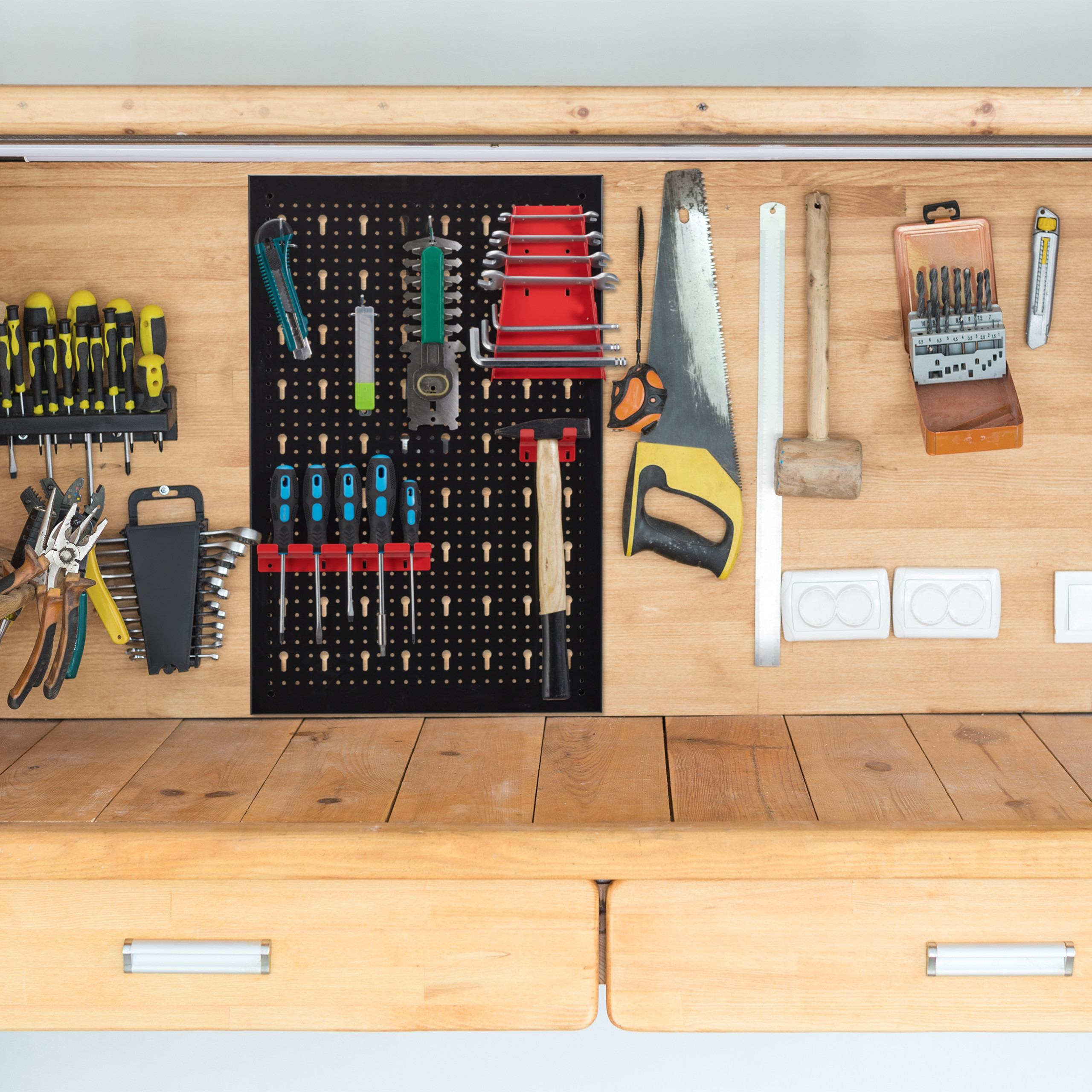 Eine Werkbank aus Holz mit verschiedenen Werkzeugen, die an einer Lochwand und einem Regal ordentlich organisiert sind.