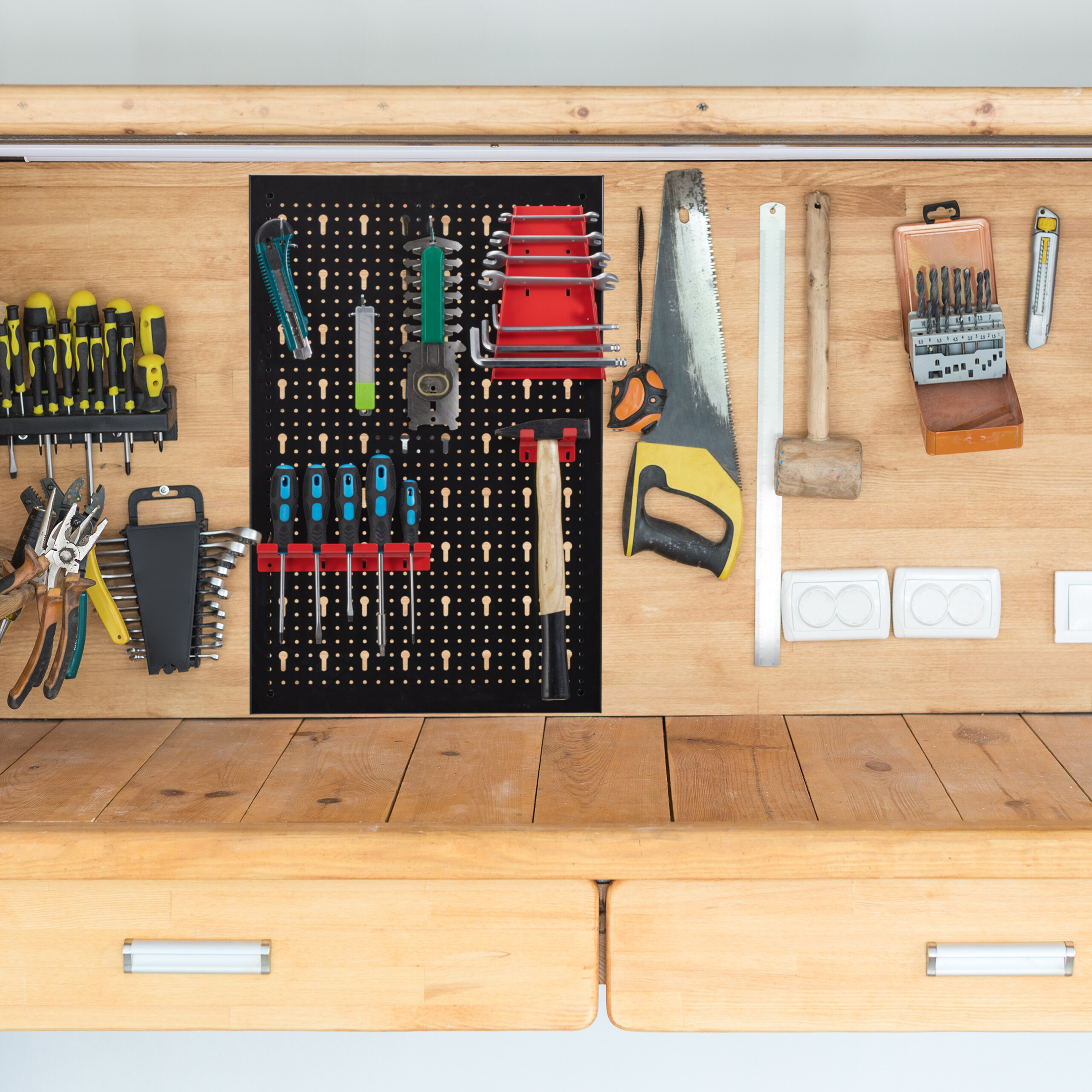 Eine Werkbank aus Holz mit an der Wand aufgehängten Werkzeugen wie Sägen, Hämmern, Zangen und Schraubendrehern.