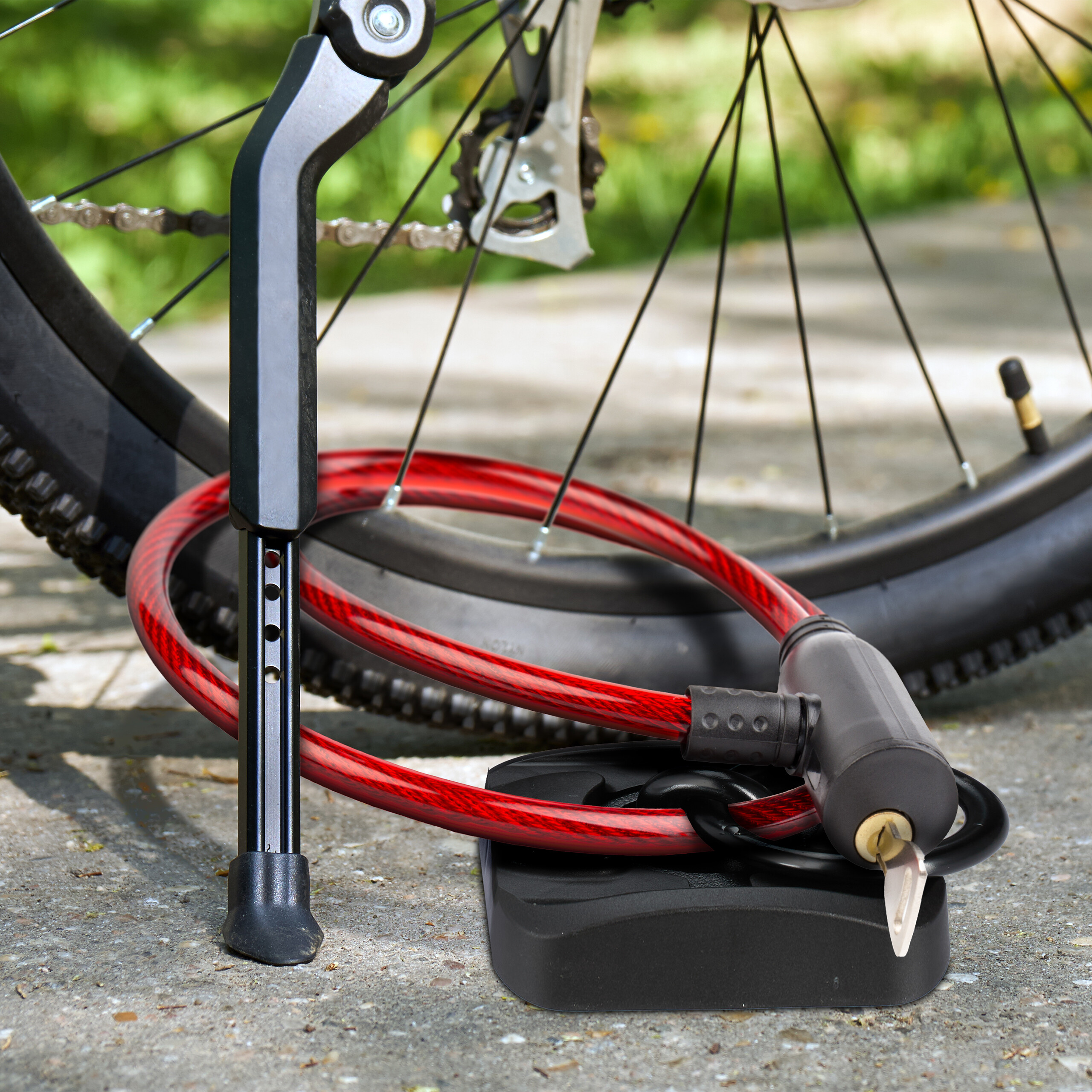 Ein rotes Spiralkabelschloss liegt am Boden vor einem Fahrradständer und Reifen.