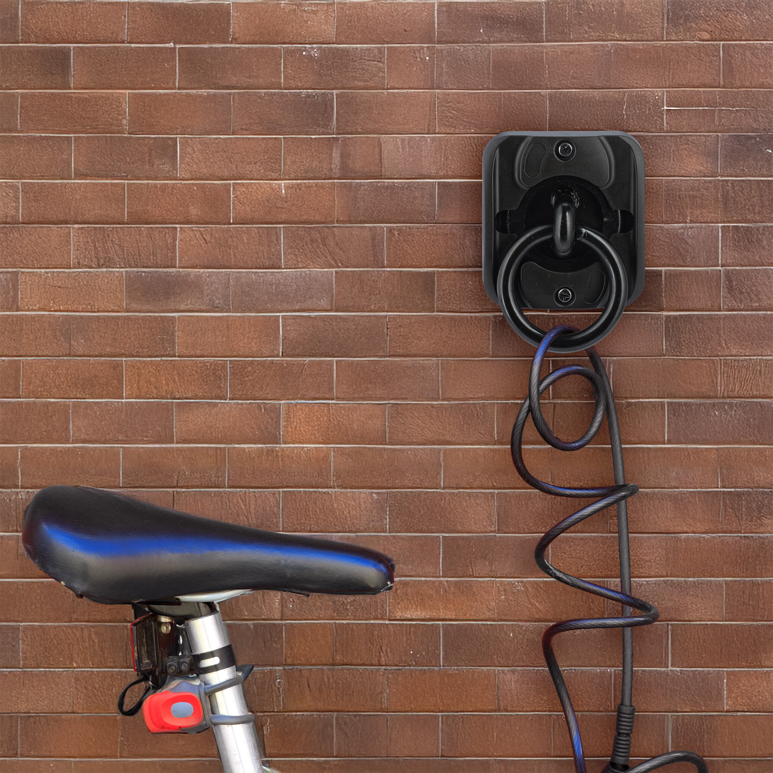 Ein Fahrradsattel und ein schwarzes Kabelschloss hängen an einer Ziegelwand.