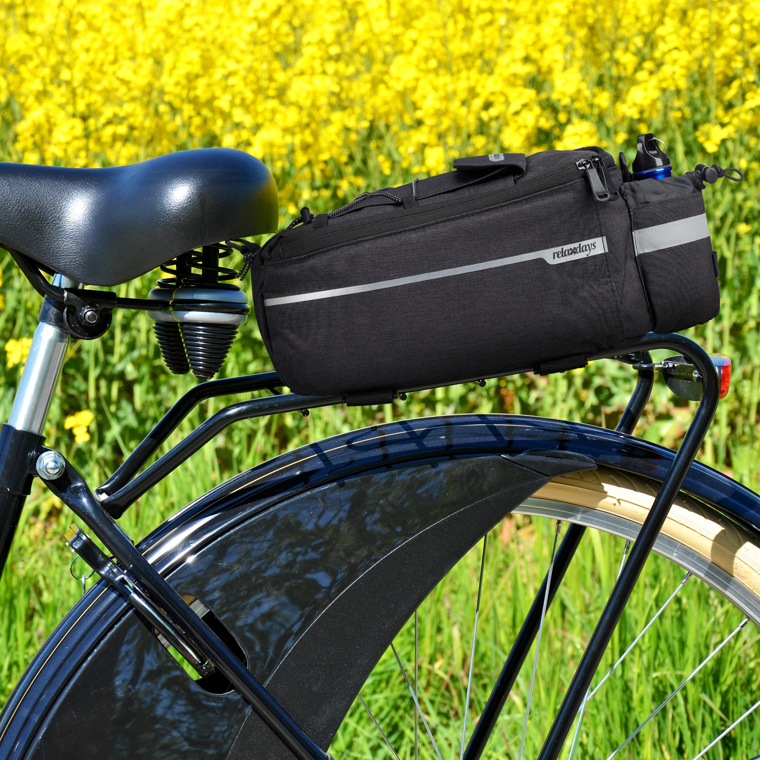 Eine schwarze Fahrradtasche auf dem Gepäckträger vor einem gelben Rapsfeld.