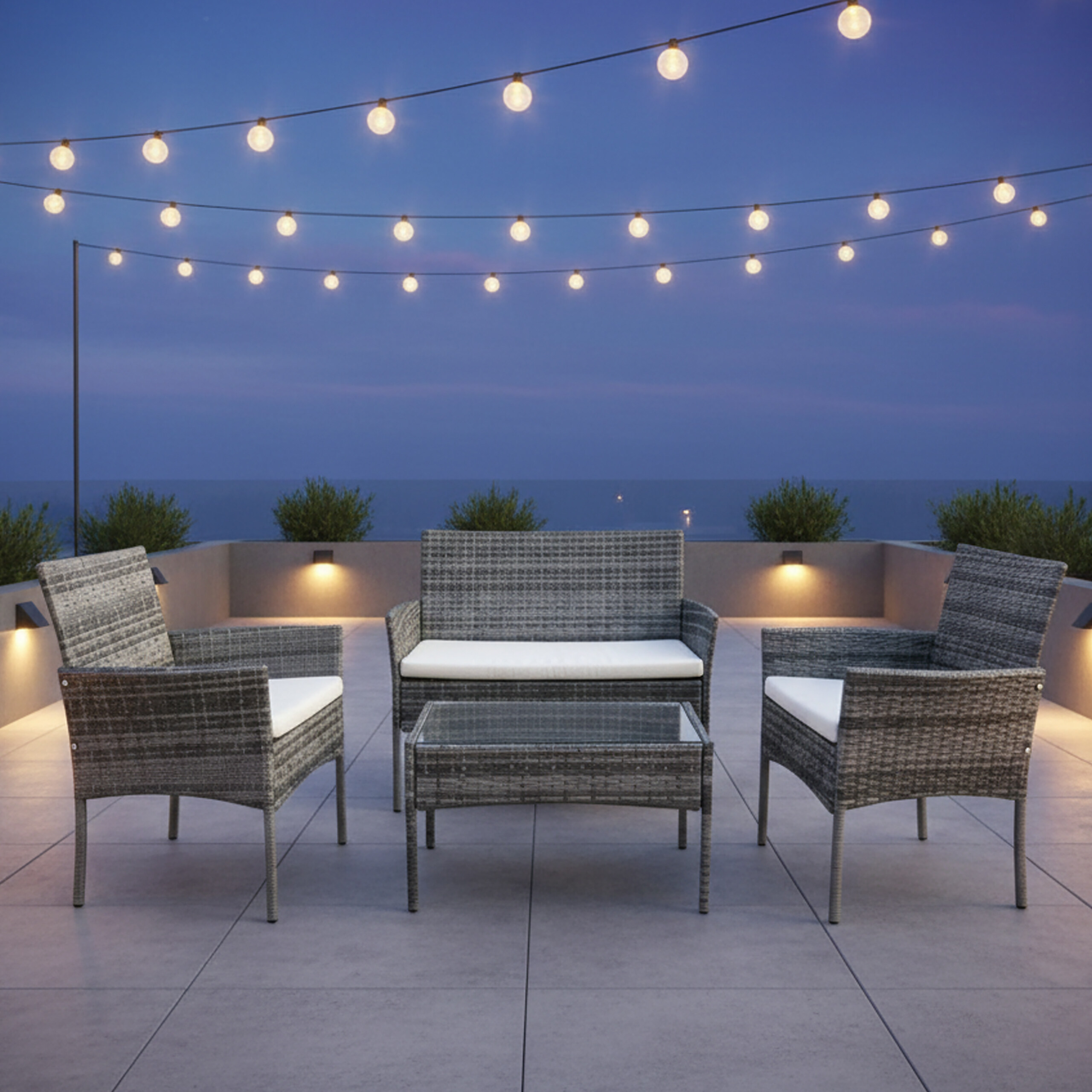 Moderne graue Rattanmöbel auf einer Dachterrasse bei Dämmerung, beleuchtet von Lichterketten.