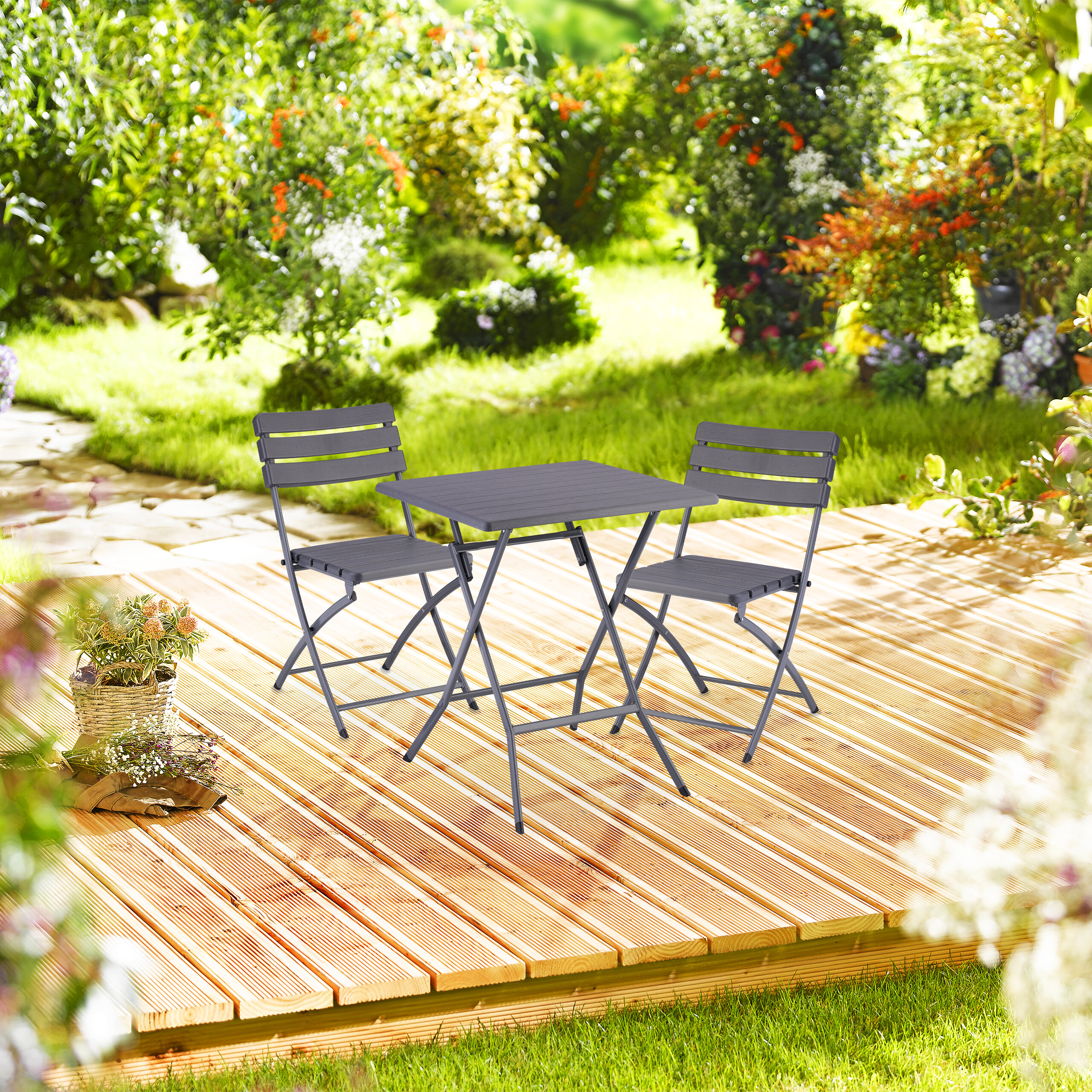 Ein grauer Klapptisch und zwei passende Stühle stehen auf einer Holzterrasse im Garten.