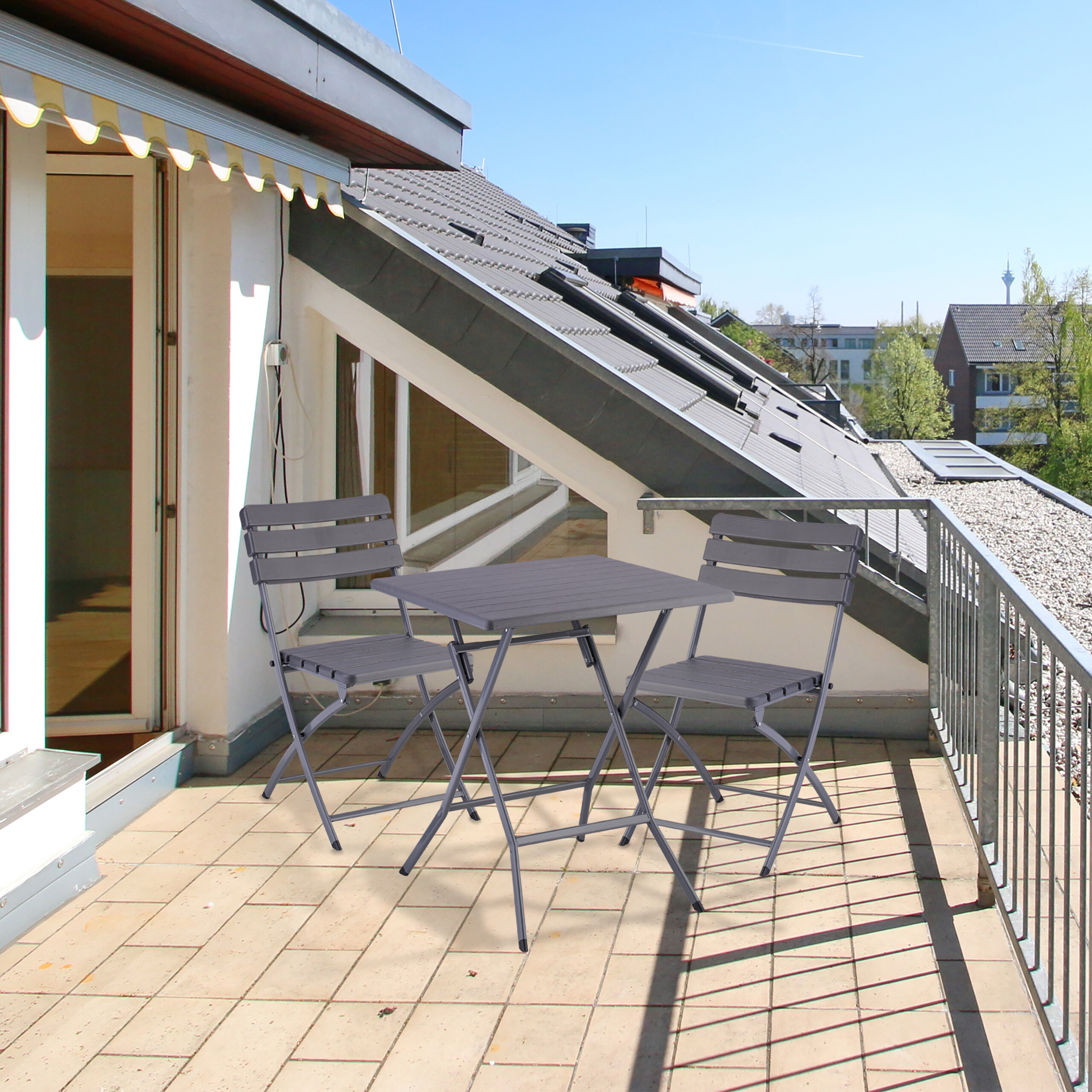 Ein grauer Klapptisch mit zwei Stühlen auf einer sonnigen Dachterrasse.