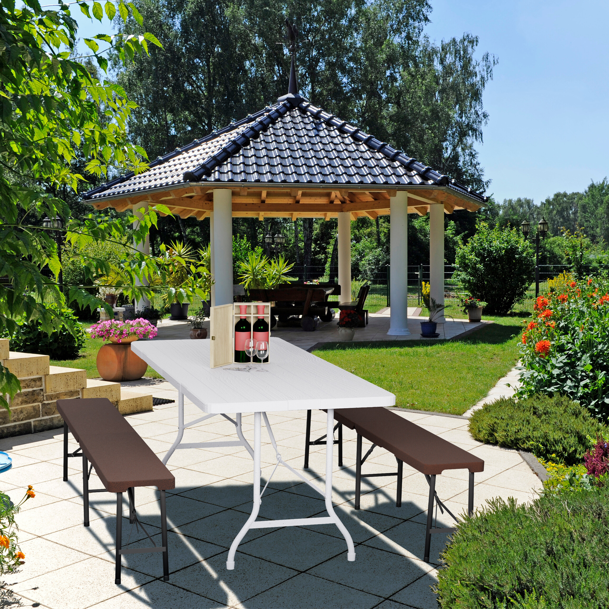 Ein weißer Tisch mit Bänken steht auf einer Terrasse vor einem Pavillon in einem Garten.