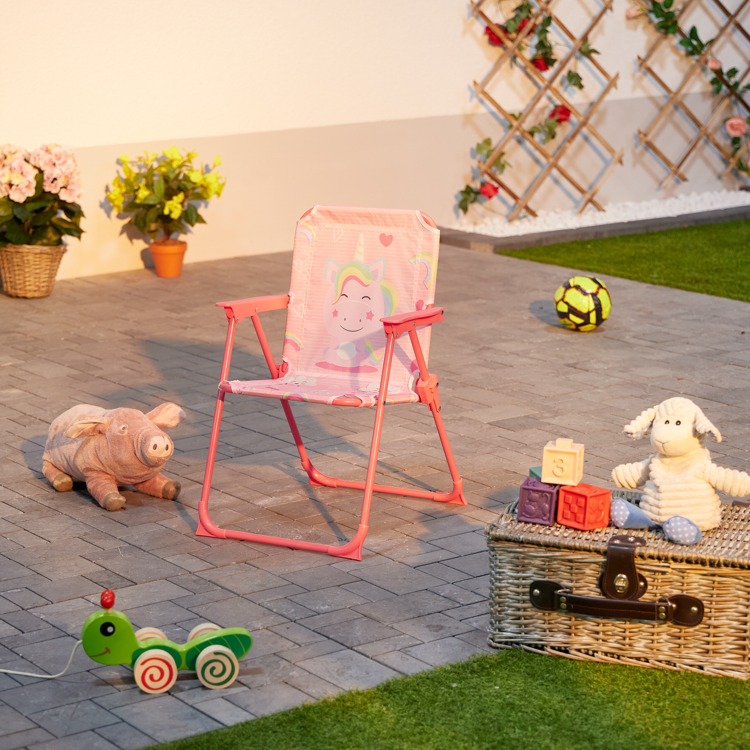 Rosa Einhorn-Klappstuhl im Garten mit Plüschtieren und Holzspielzeug.