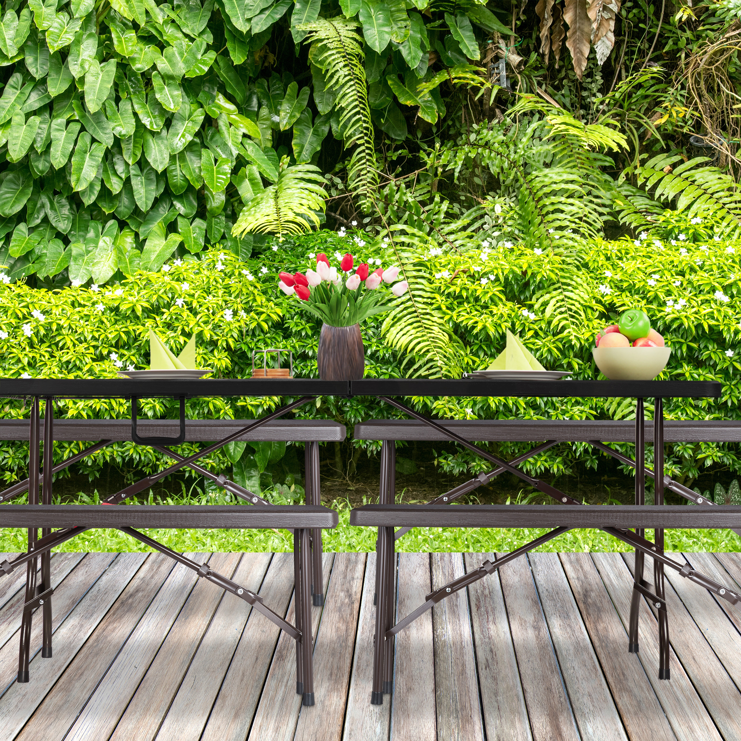 Ein Holztisch mit roten Tulpen, Tellern und Obstschale steht auf einer Holzterrasse vor einem grünen Garten.