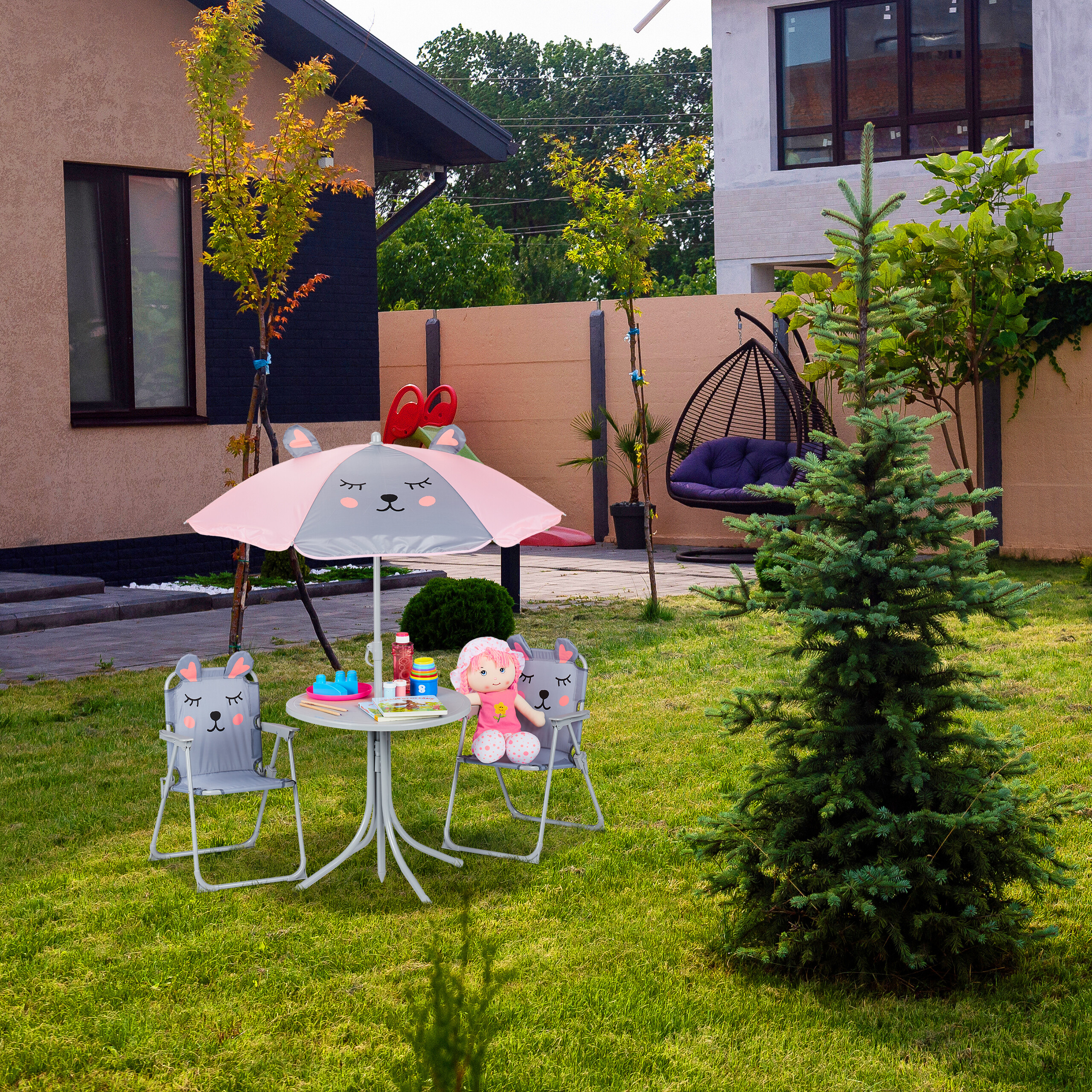 Ein Kindertisch mit Sonnenschirm und passenden Stühlen auf einem Gartenrasen vor einem Haus.